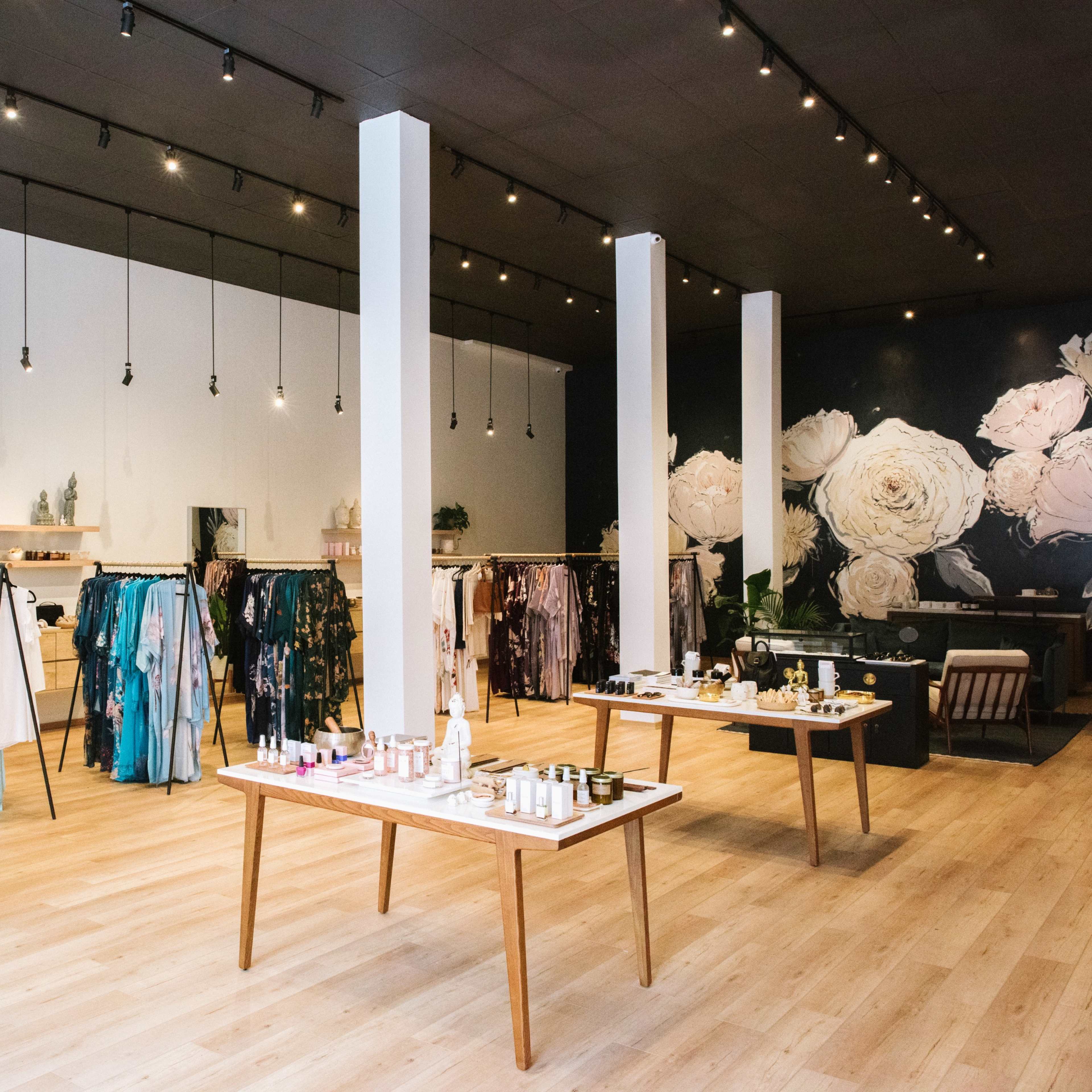 A boutique with clothing racks displaying colorful garments and tables featuring various beauty products in a well-lit space.