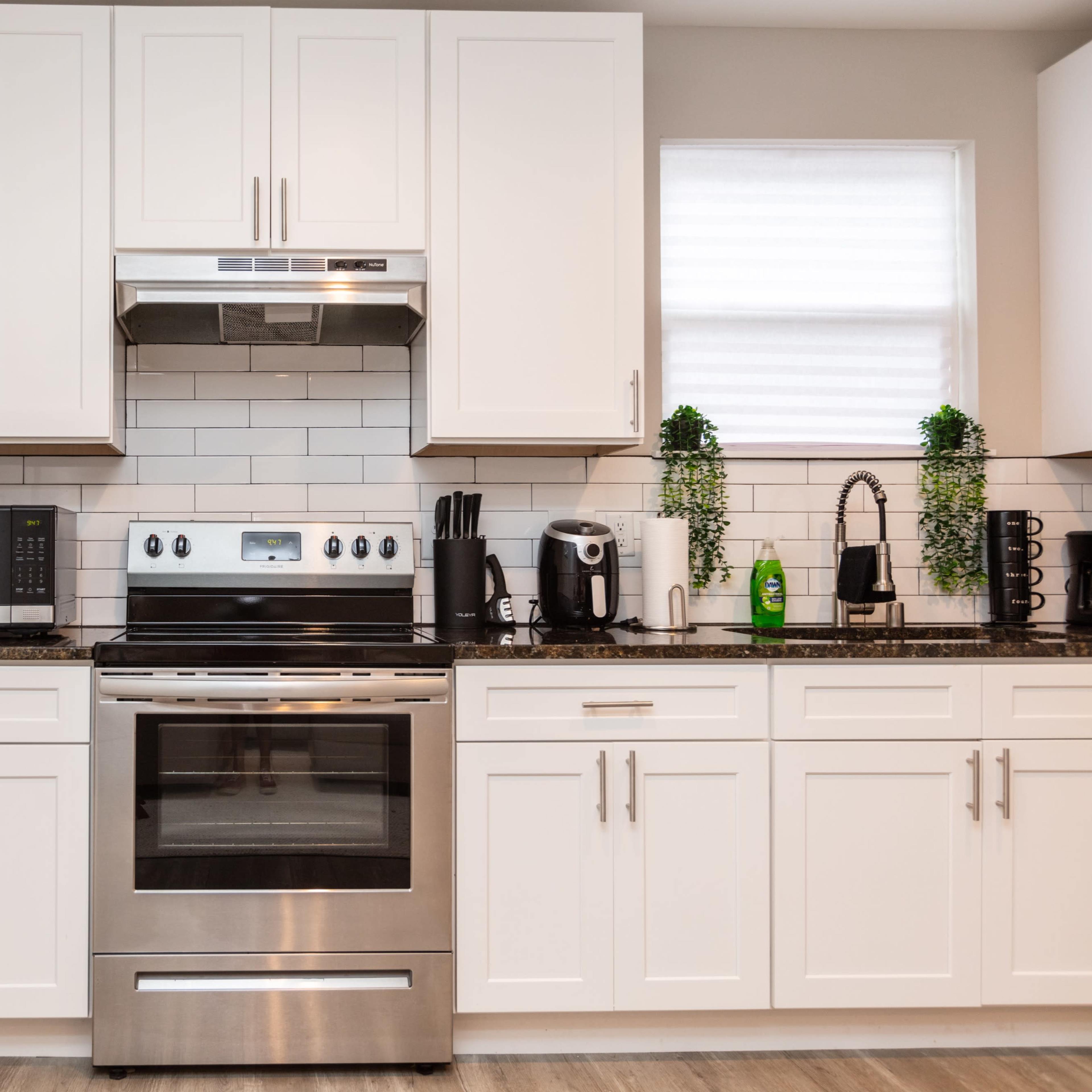 A modern kitchen features stainless steel appliances, including an oven, microwave, and coffee maker, against white cabinetry and a tiled backsplash.