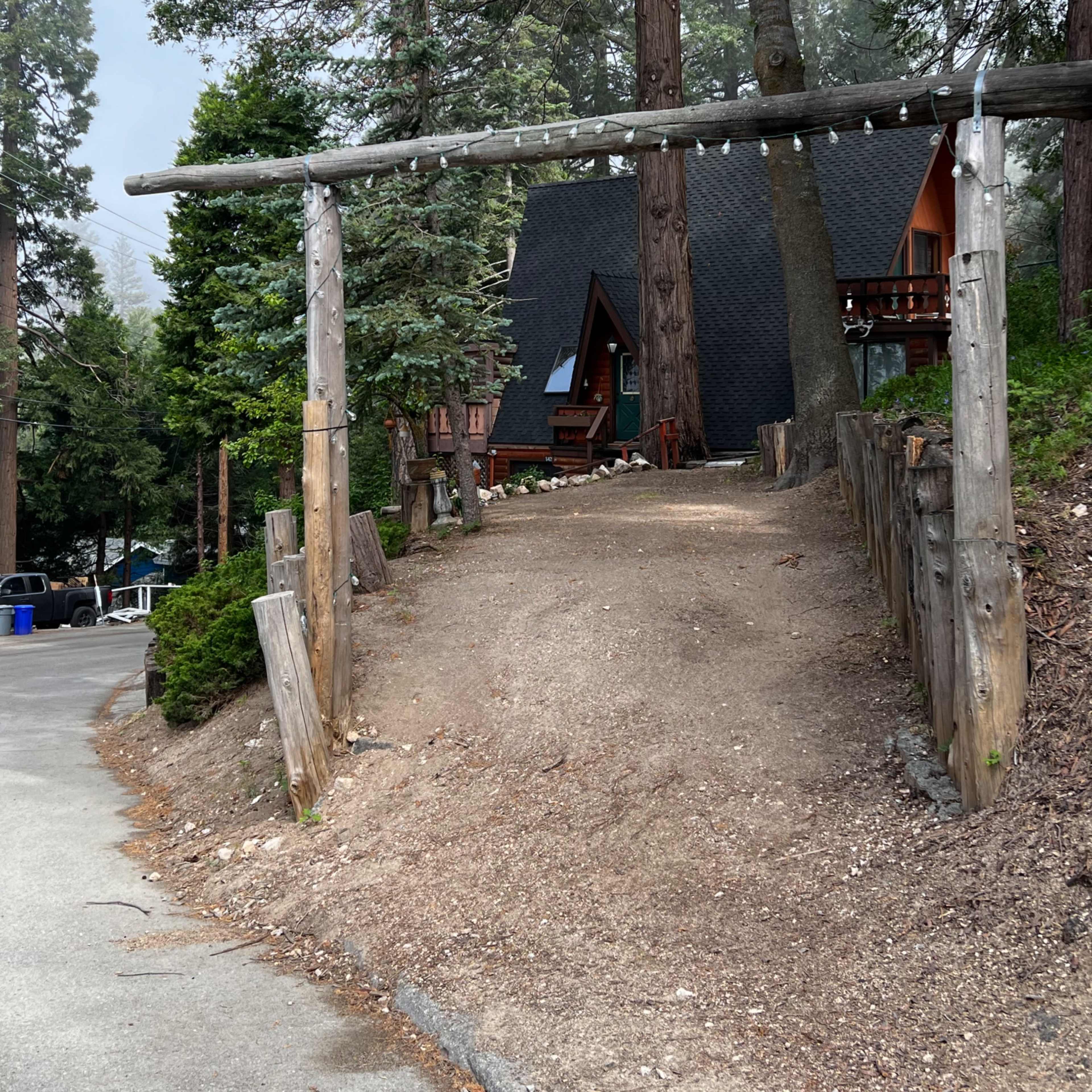 A gravel path leads to an A-frame cabin surrounded by tall trees.