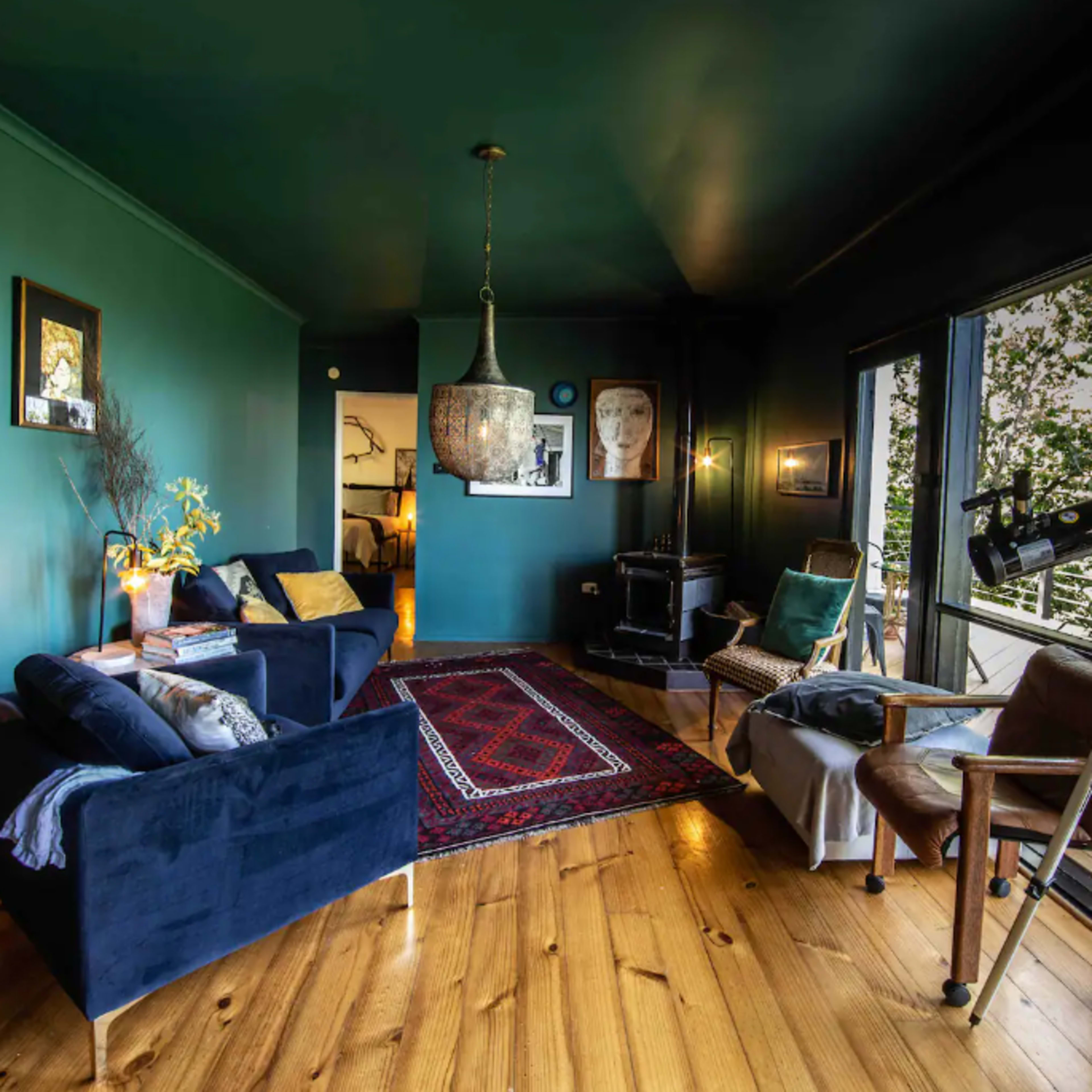 The room features dark green walls, wooden flooring, a mix of seating arrangements, a telescope, and large windows with views of greenery outside.