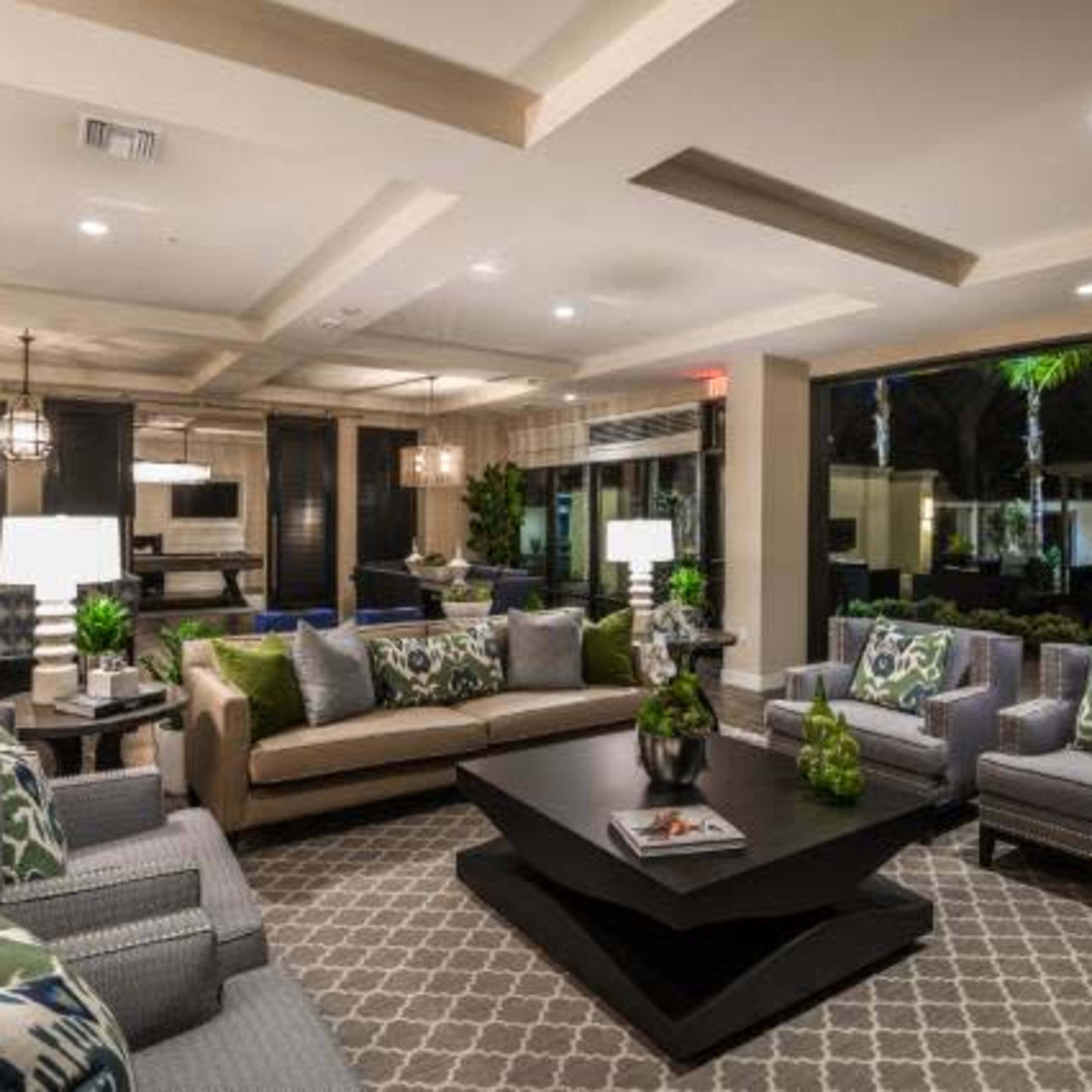 A modern living room features comfortable seating arrangements, a central coffee table, and large windows allowing natural light to illuminate the space.