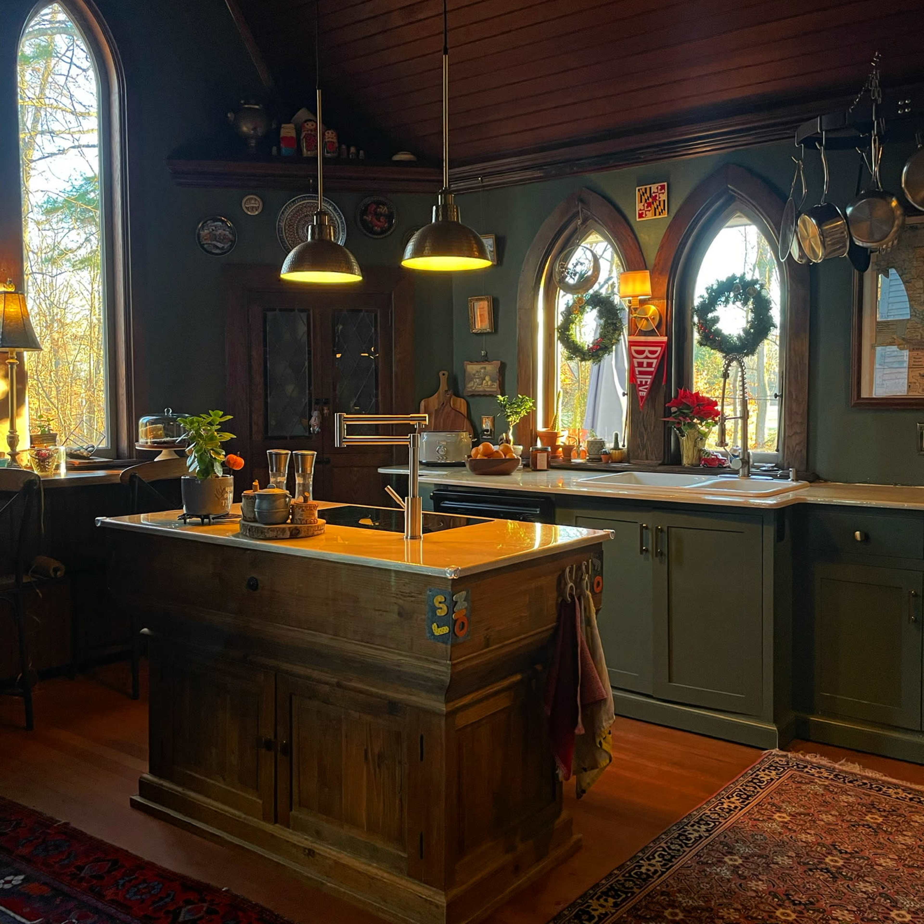 The kitchen features a wooden island with a sink, surrounded by dark green cabinetry and large windows that let in natural light.