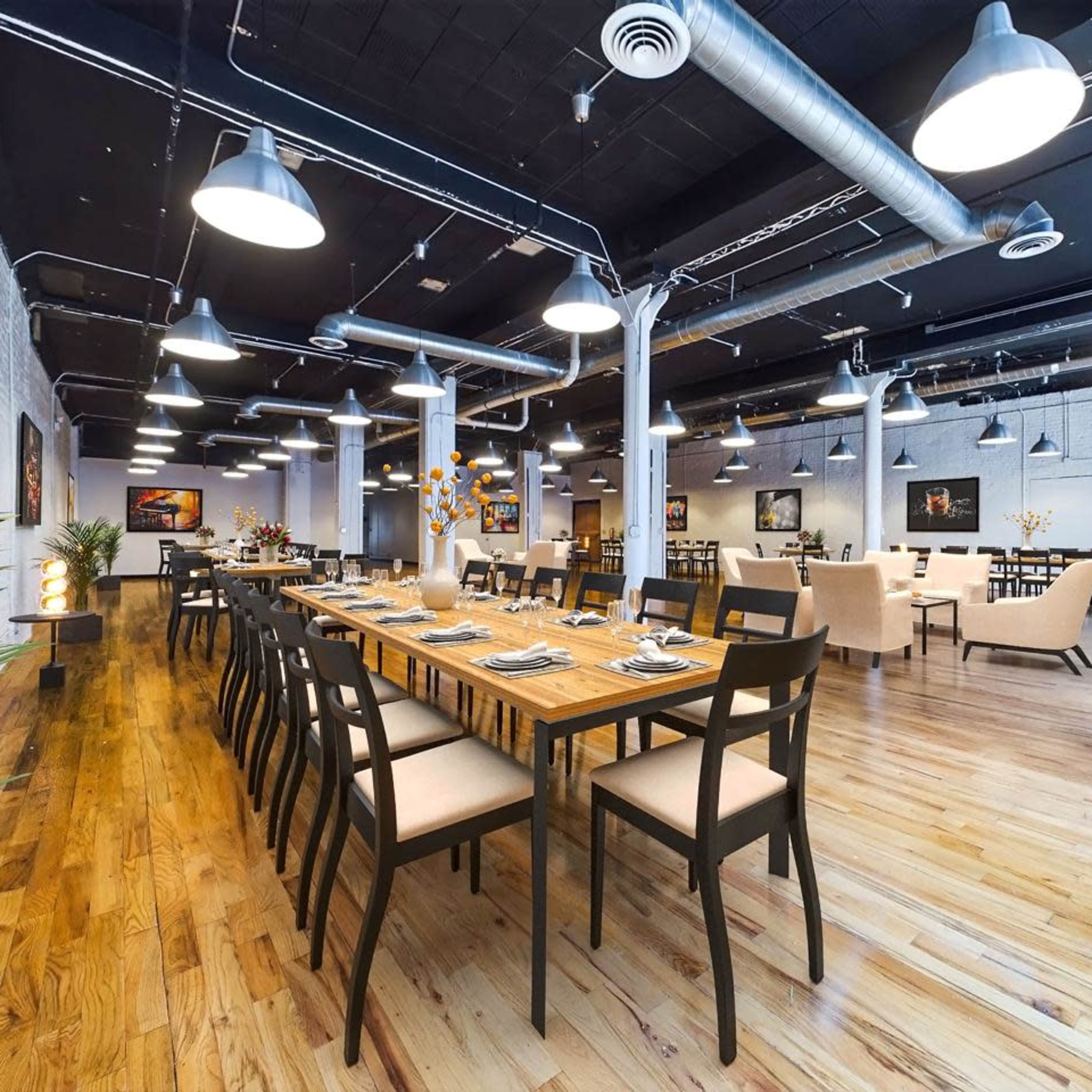 A spacious restaurant featuring wooden tables with chairs, pendant lighting, and artwork on the walls.