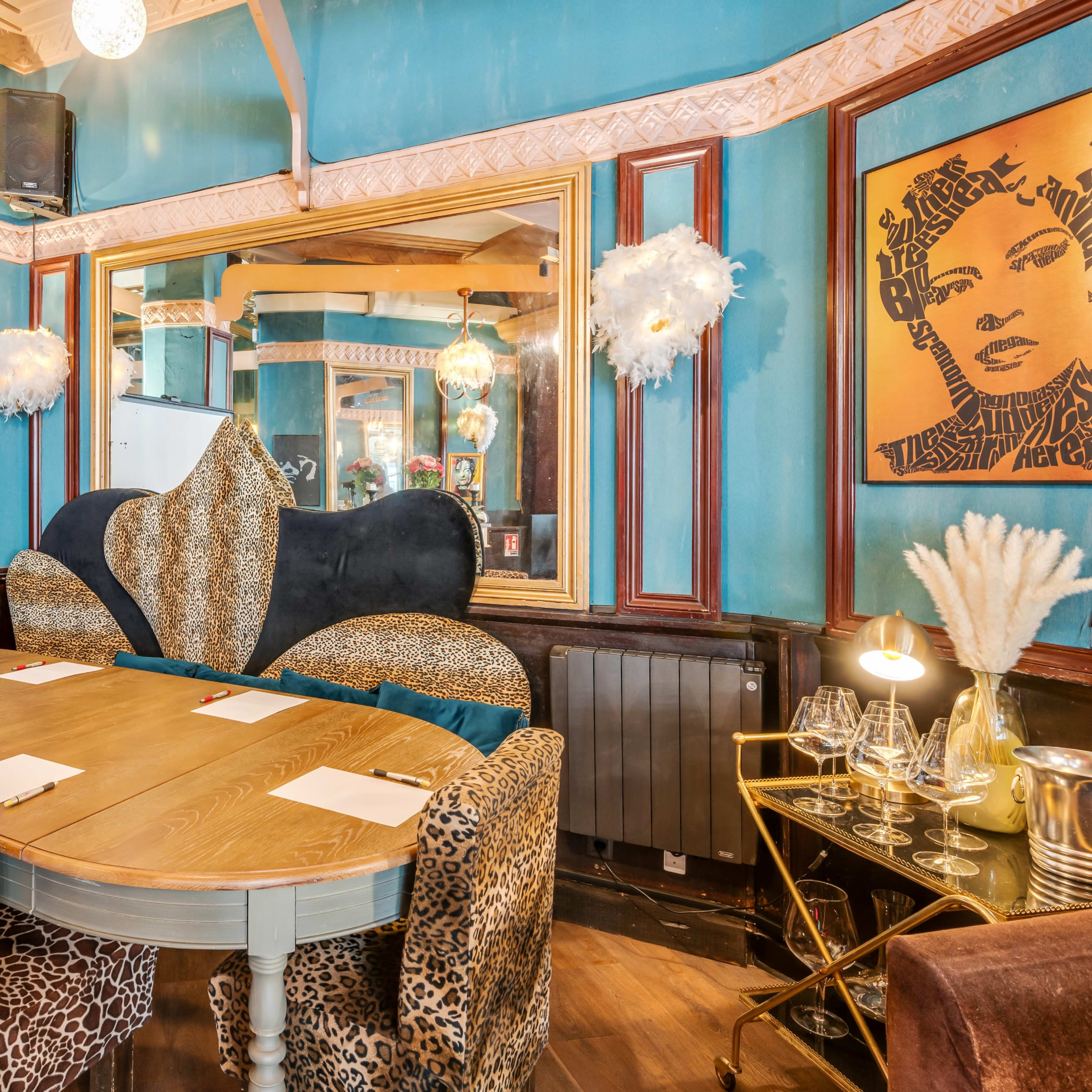 A dining area with a large round table surrounded by various patterned chairs, a projector screen, and colorful walls adorned with mirrors and artwork.