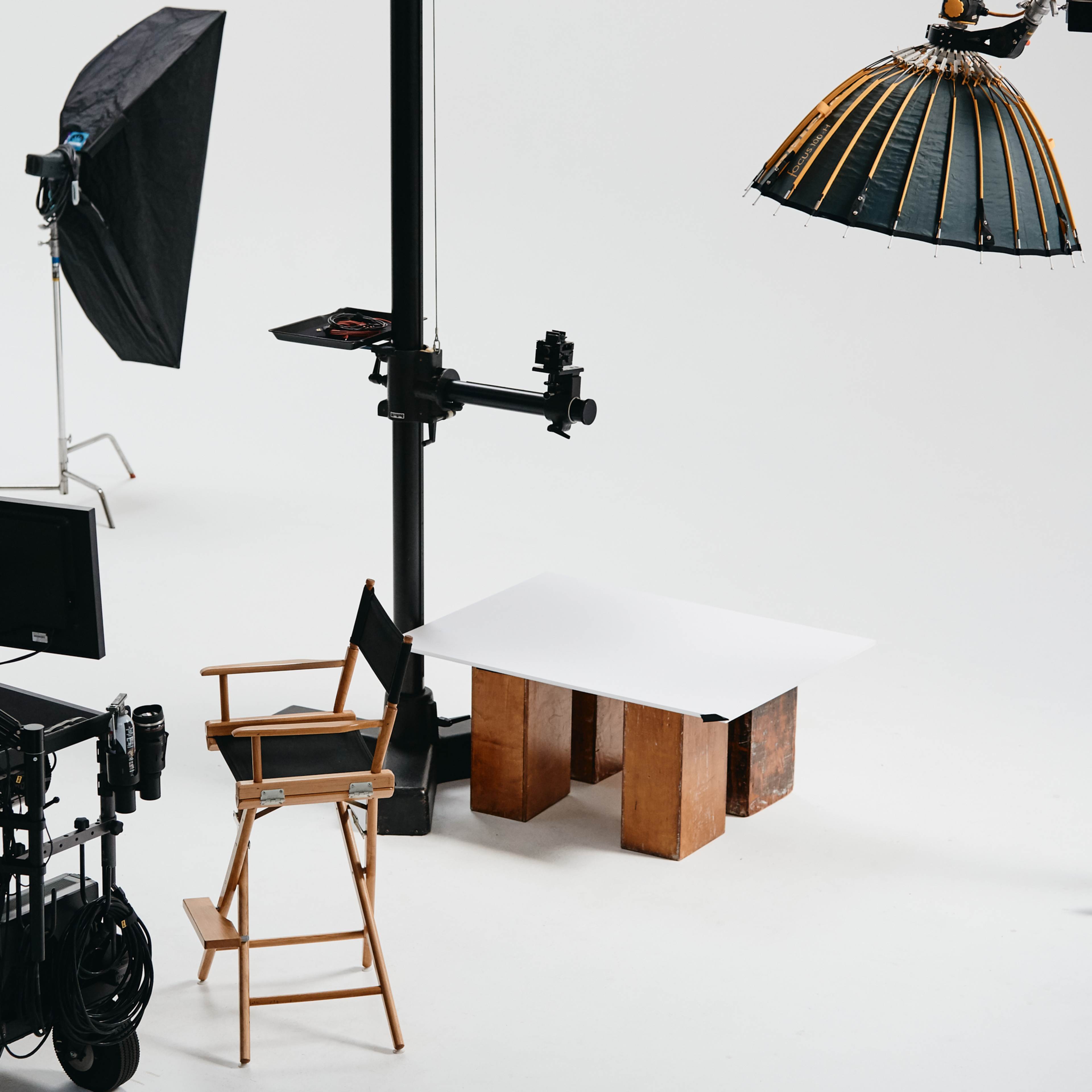 A photography studio setup with a director's chair, a table made of wooden crates, and large lighting equipment overhead.
