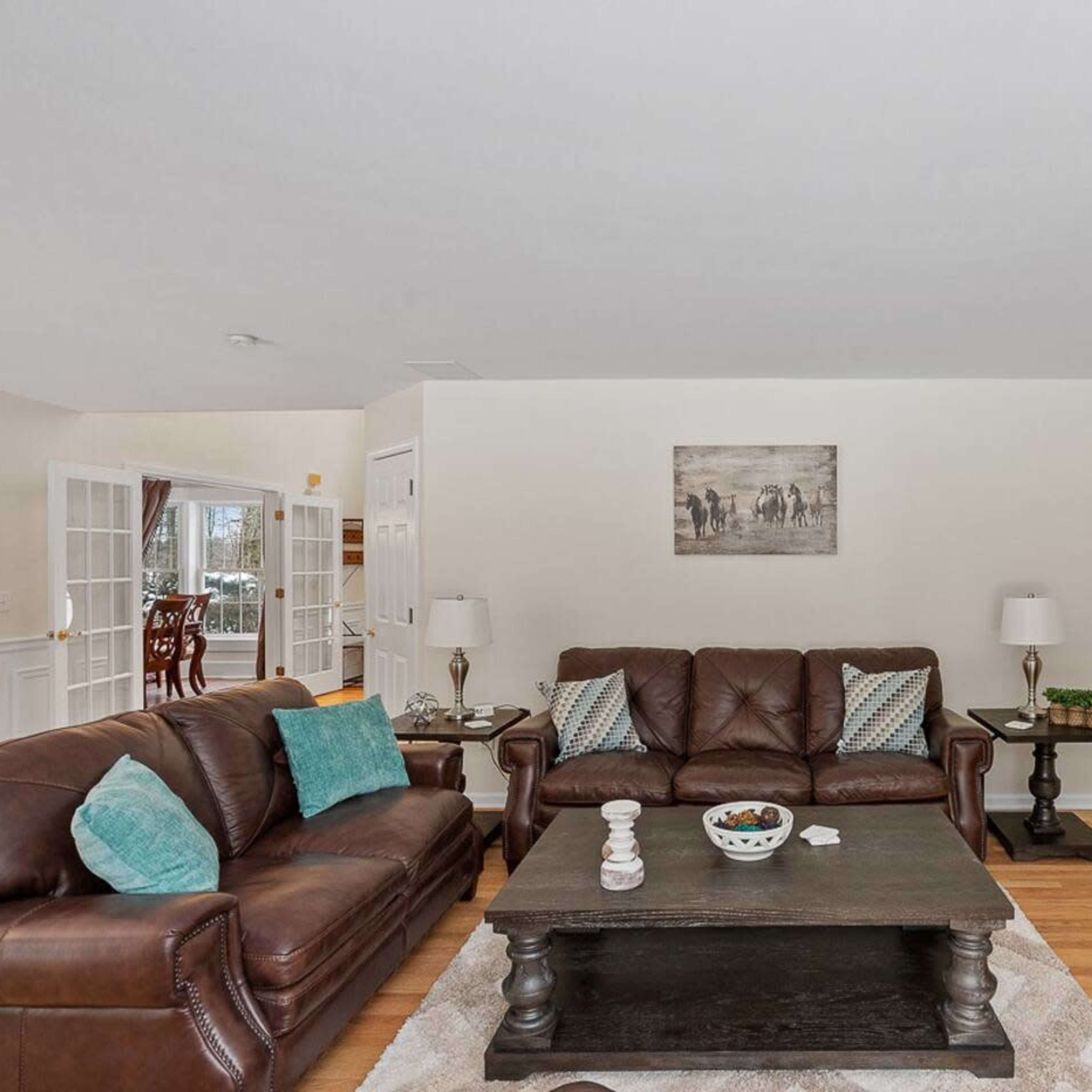 A living room features two brown leather sofas, a wooden coffee table, and a fireplace, with light-colored walls and a large flat-screen TV.