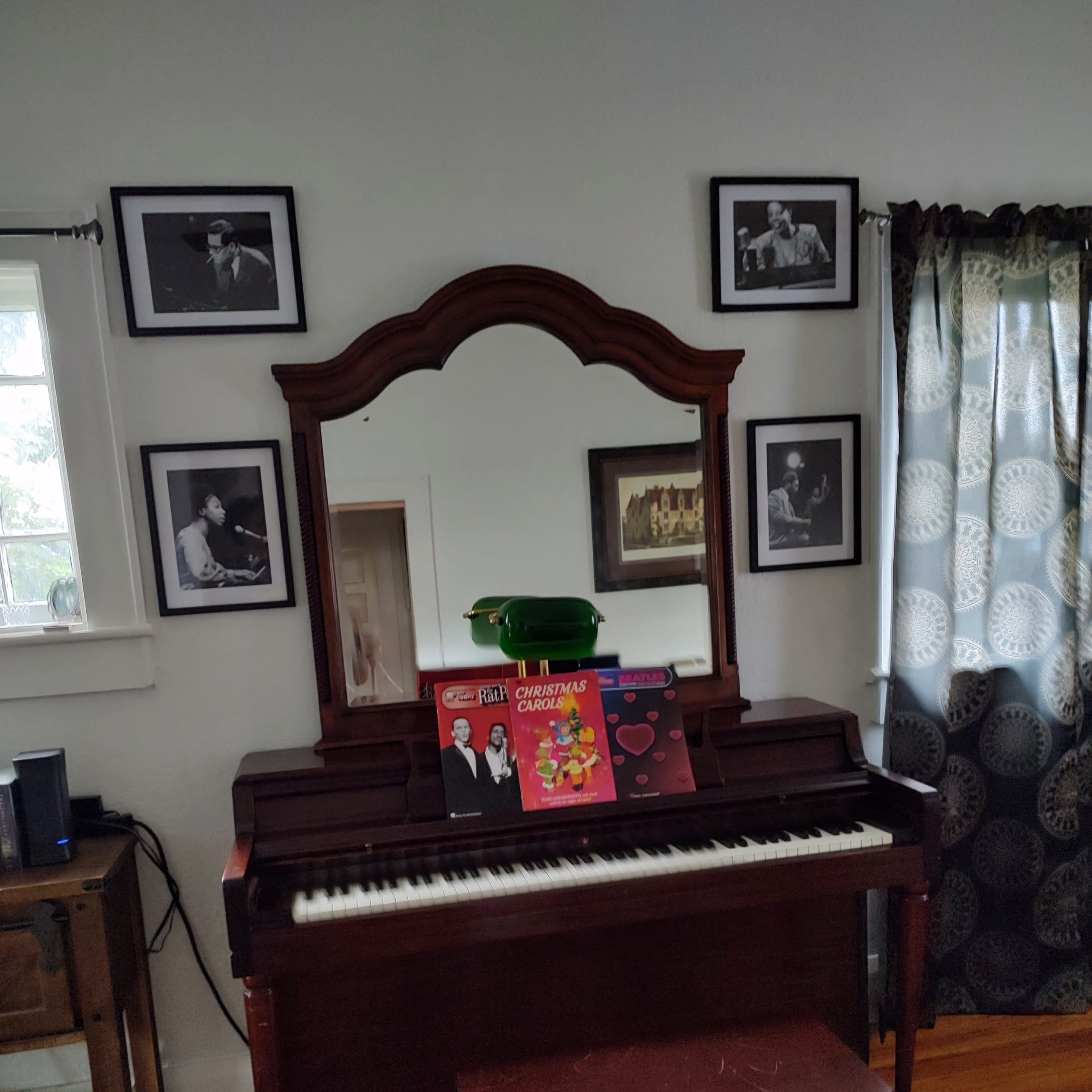 A vintage piano with sheet music and records displayed on top is positioned against a wall adorned with framed black-and-white photographs.