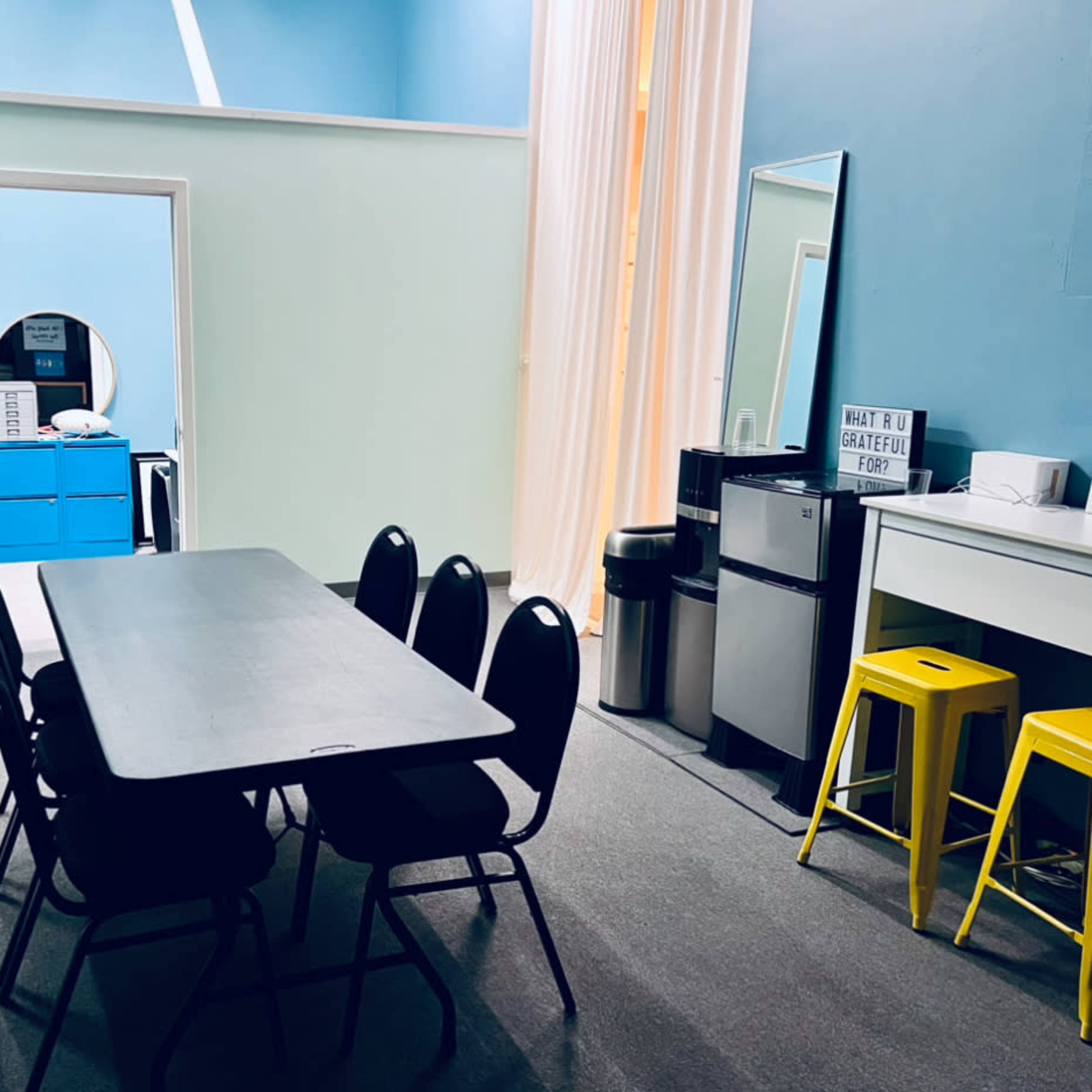 A conference room with a large table surrounded by six black chairs, a blue cabinet, and a mirror on the wall.