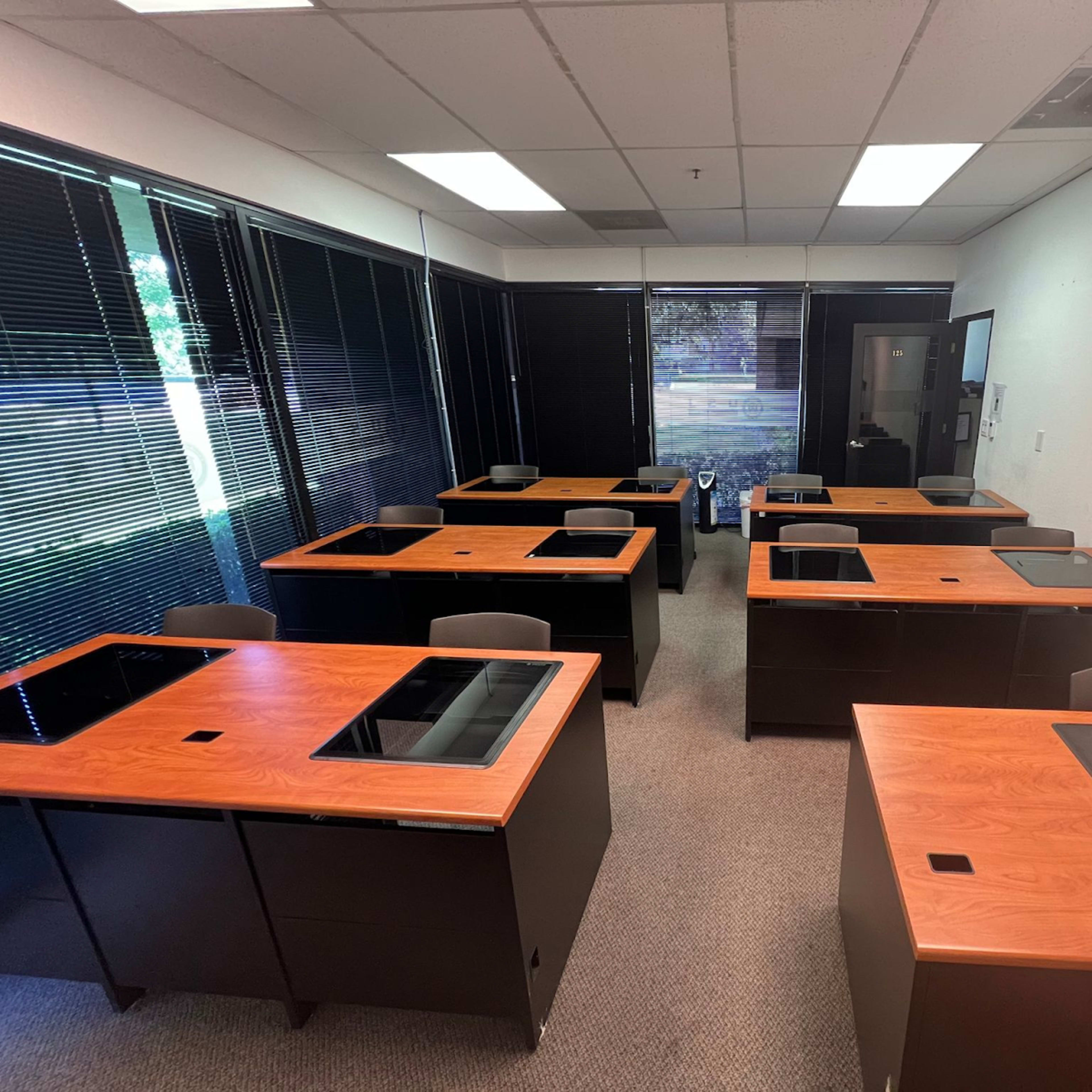 A classroom or office space with multiple desks arranged in a symmetrical layout, featuring dark cabinetry and wooden surfaces.