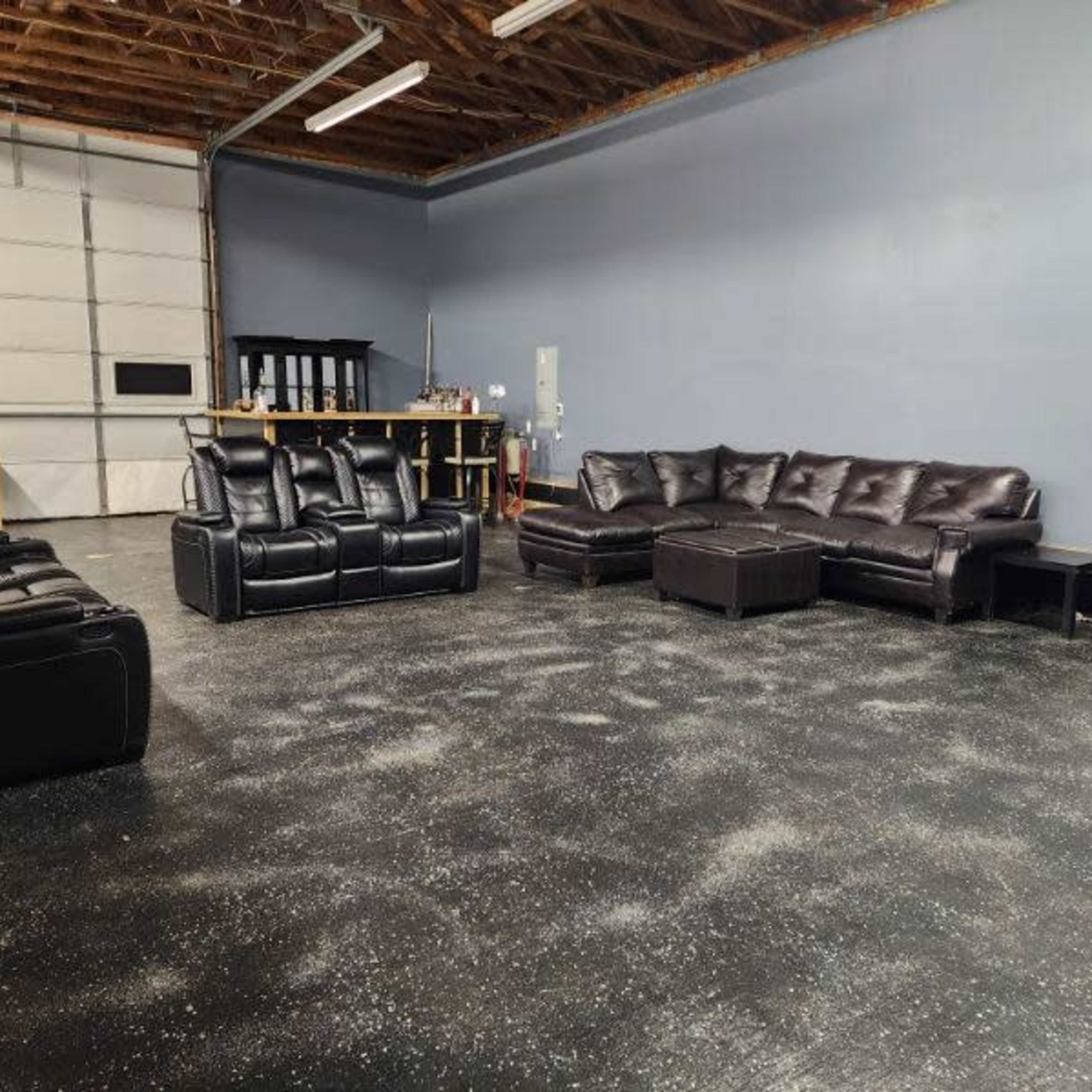 A spacious room with a polished black floor, featuring several black leather couches and a large garage door in the background.