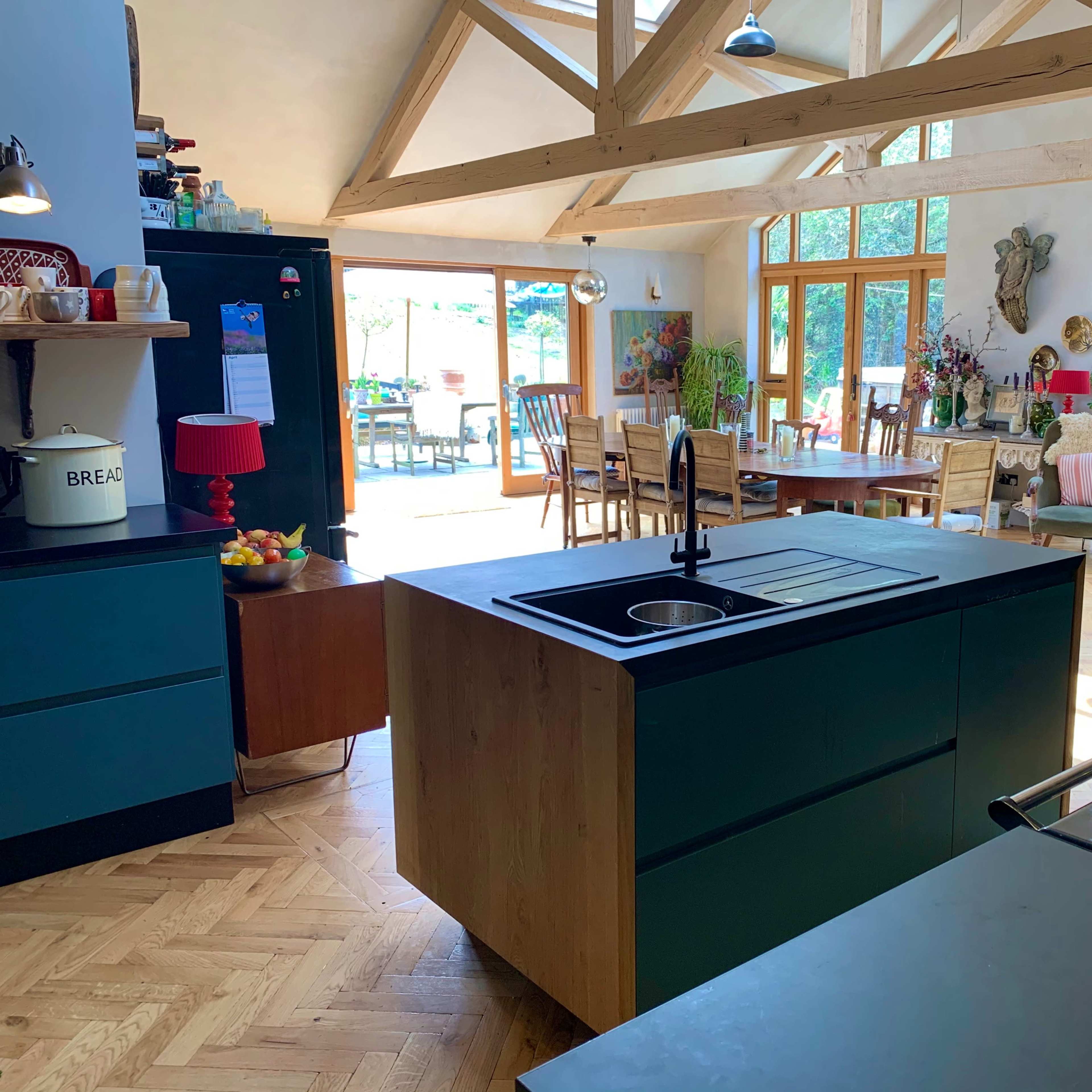 A modern kitchen with an island, featuring wooden beams and large windows that open to a dining area.