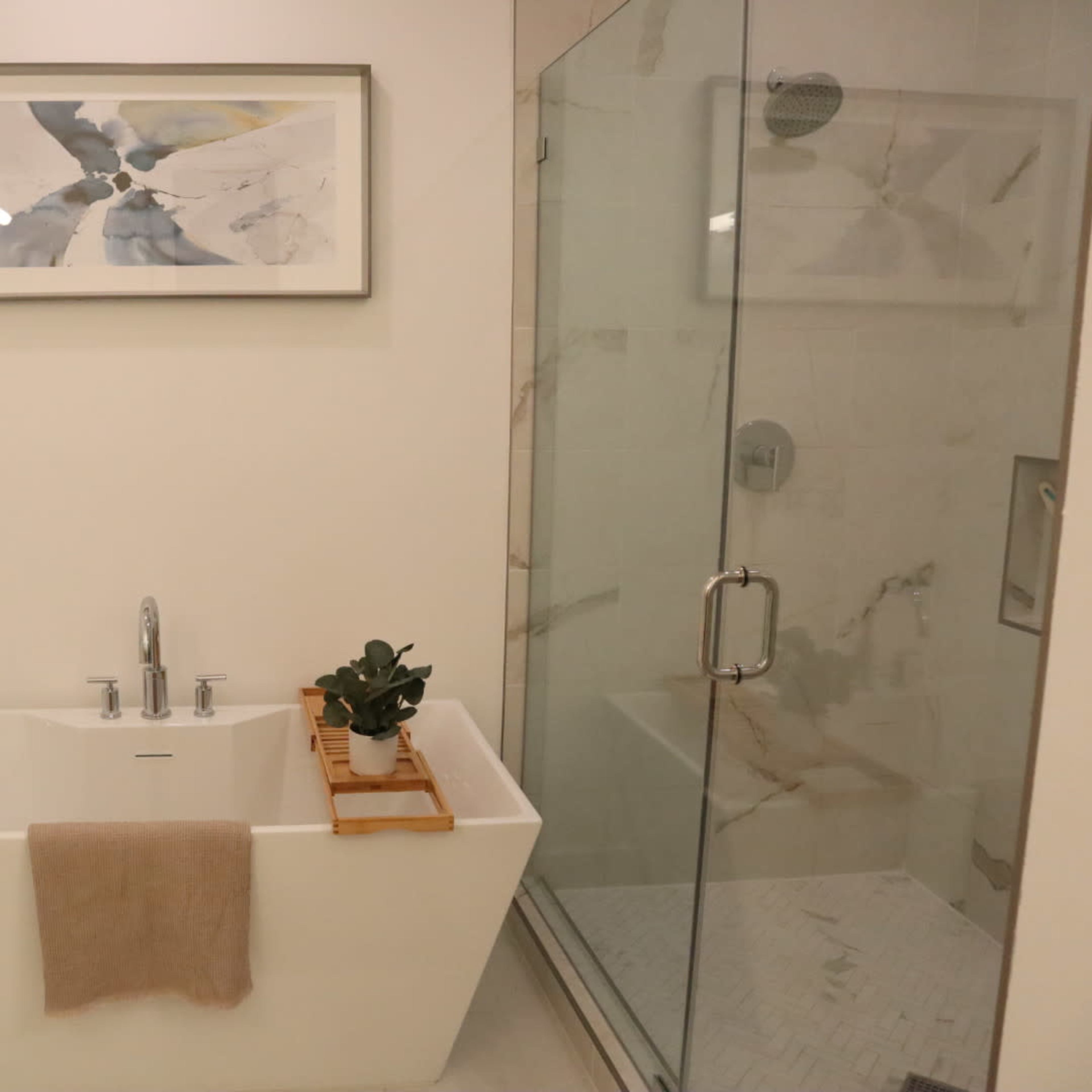 A modern bathroom featuring a freestanding bathtub, a glass shower, and a framed abstract painting on the wall.