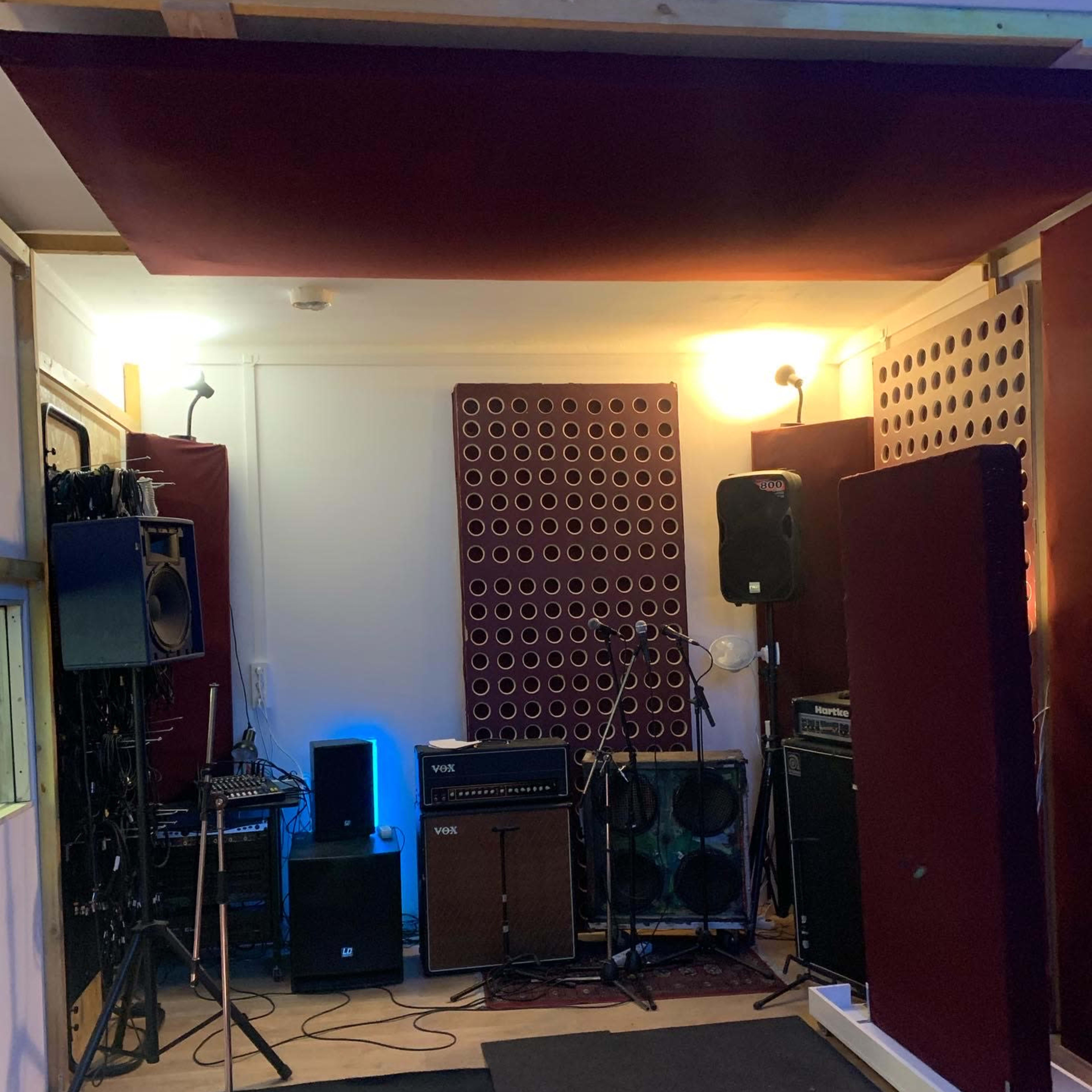 A music rehearsal studio with microphones, amplifiers, and soundproofing panels arranged in the space.