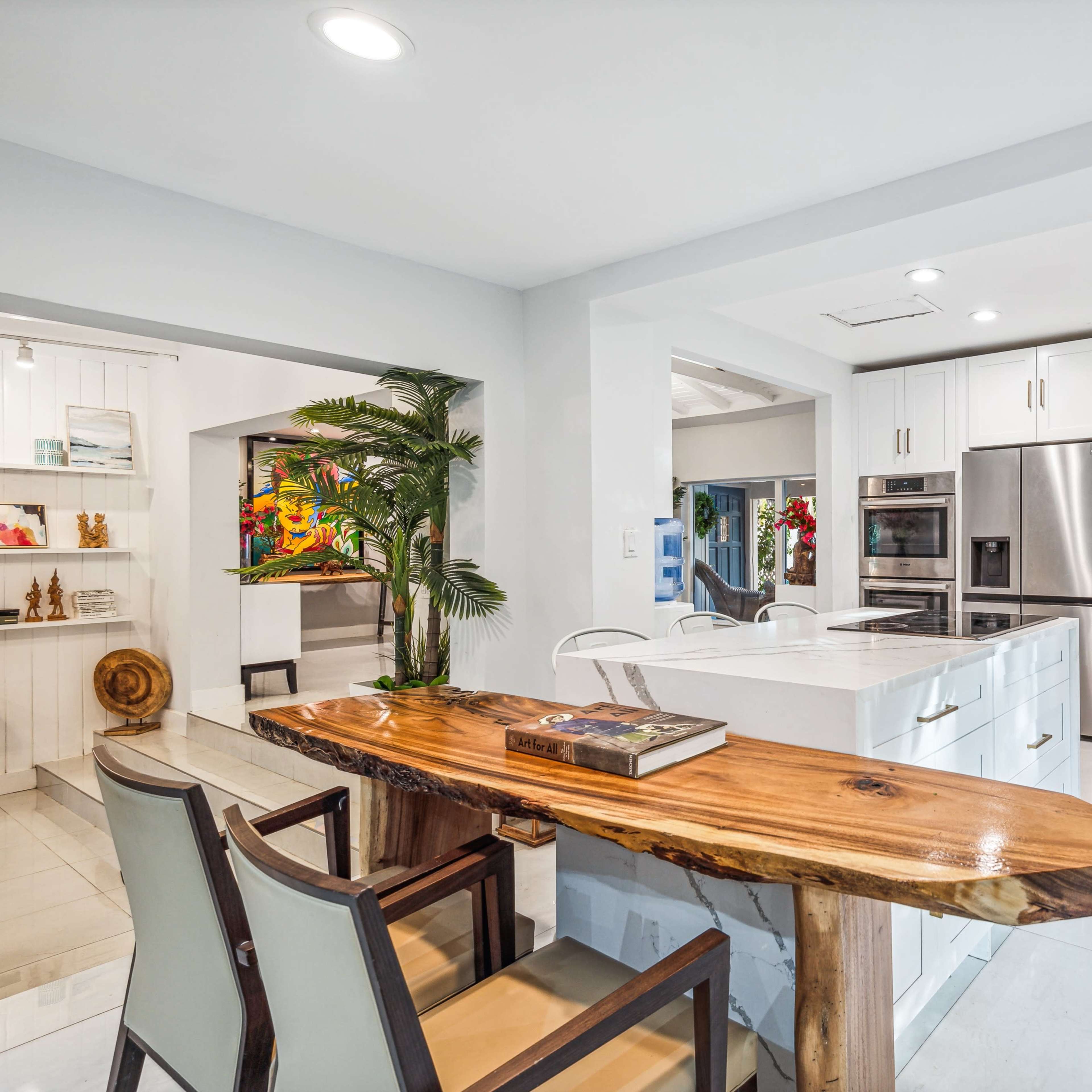 A modern kitchen with white cabinetry, a large island, and a wooden table with chairs positioned nearby.