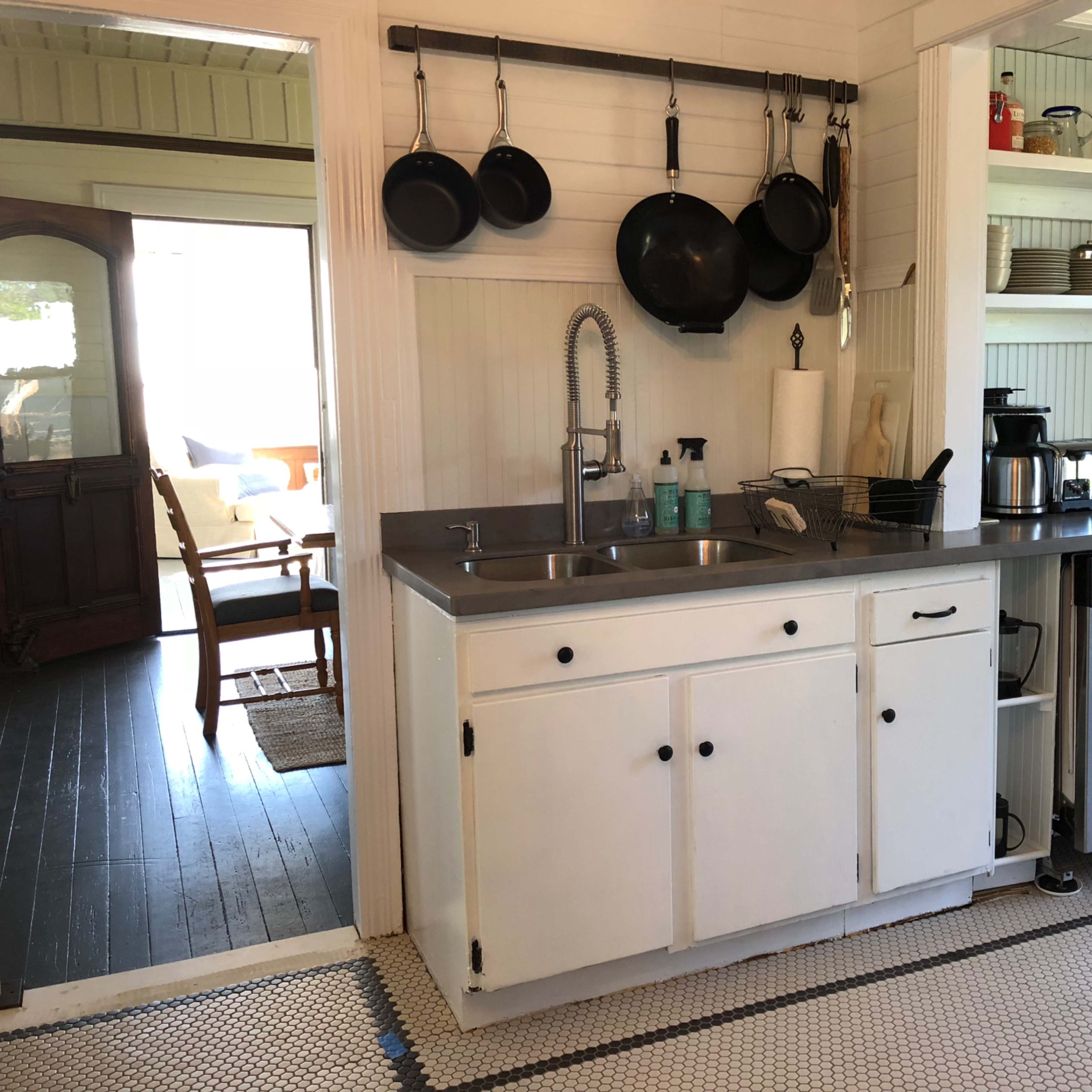 A small kitchen with a stainless steel countertop, white cabinets, hanging pots, and an array of kitchen appliances.