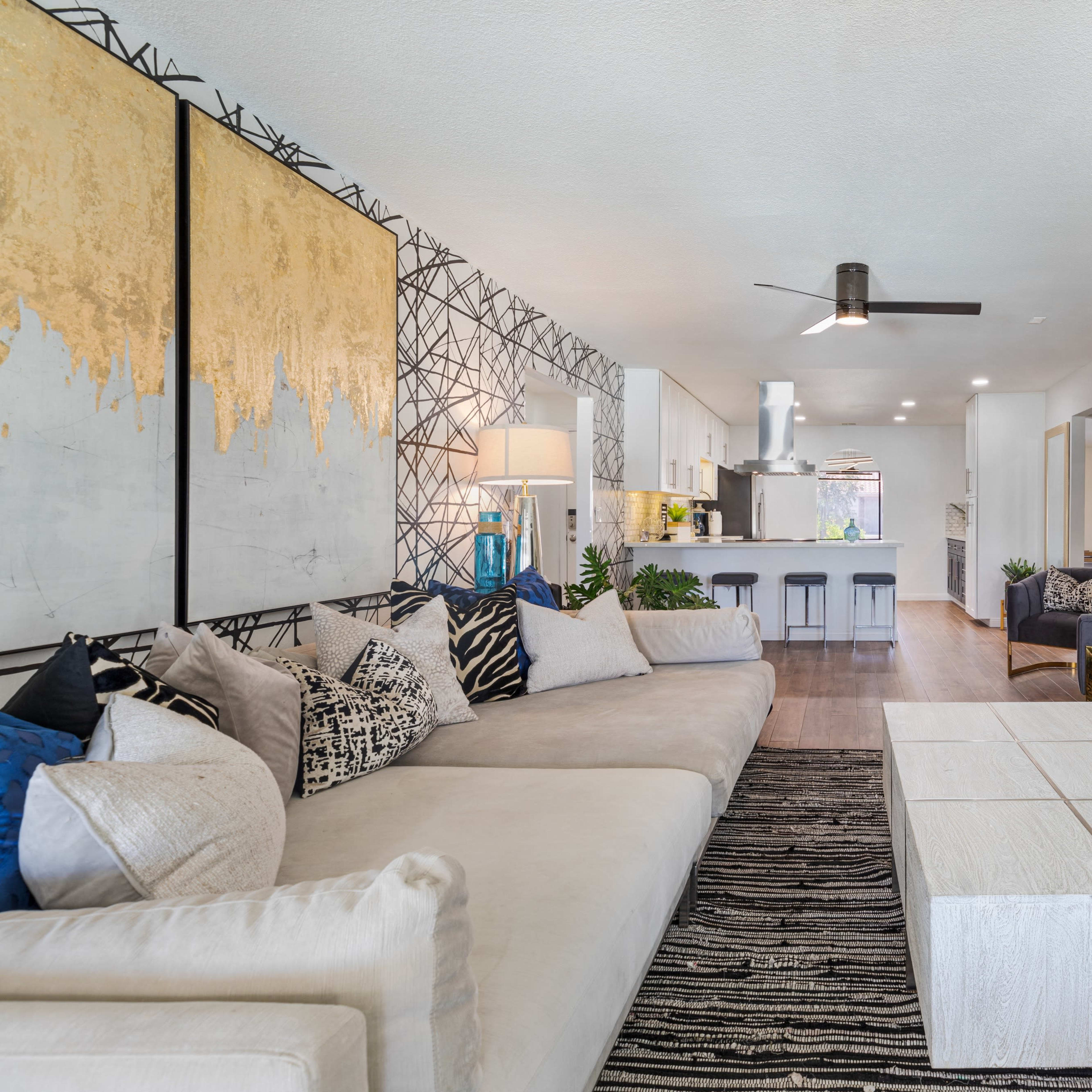 A modern living room features a sectional sofa, a striped area rug, and a sleek entertainment unit, with an open kitchen visible in the background.