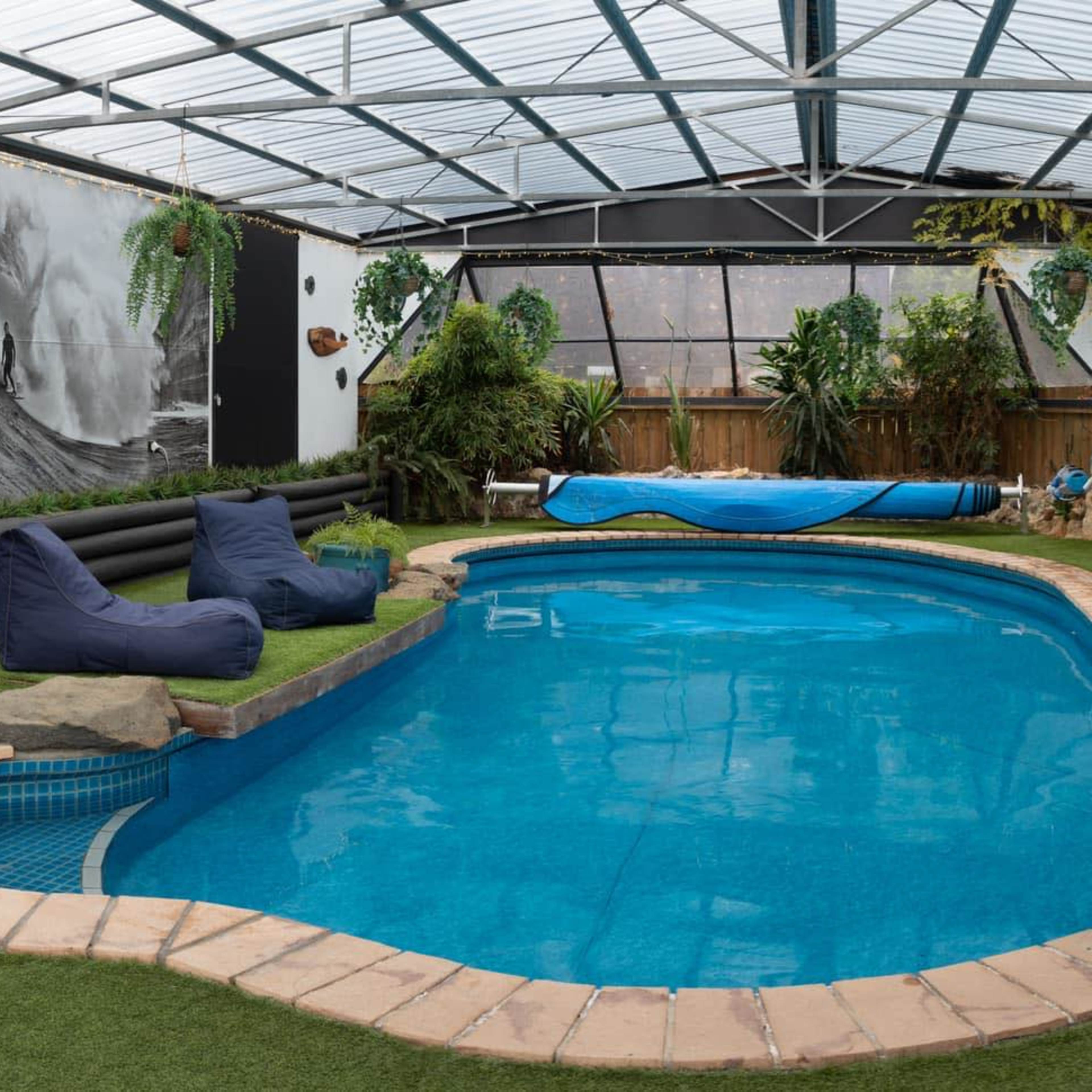 An indoor swimming pool area surrounded by green turf, bean bag seating, and a large TV on the wall.