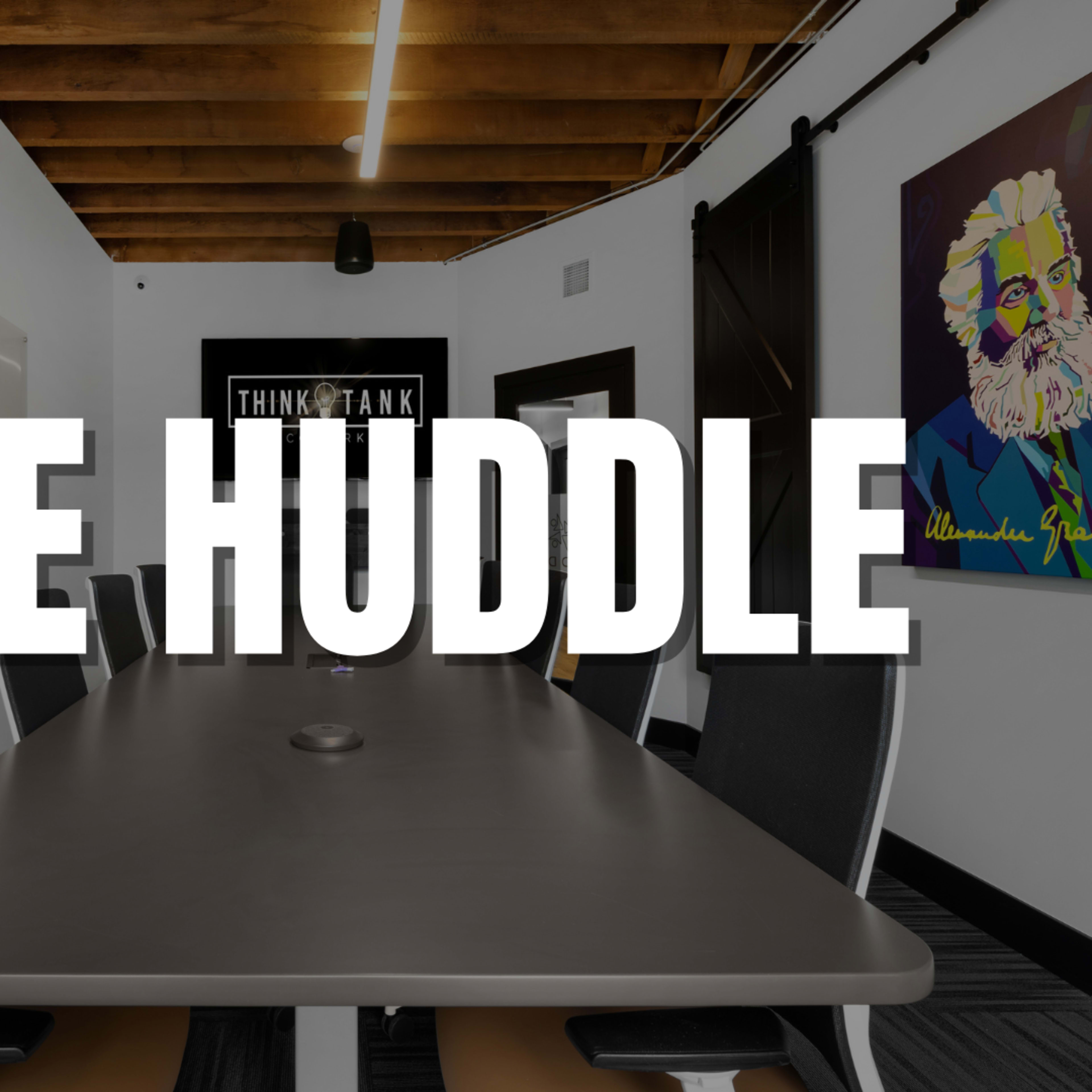 A modern conference room features a long table surrounded by chairs, with a colorful artwork on the wall.