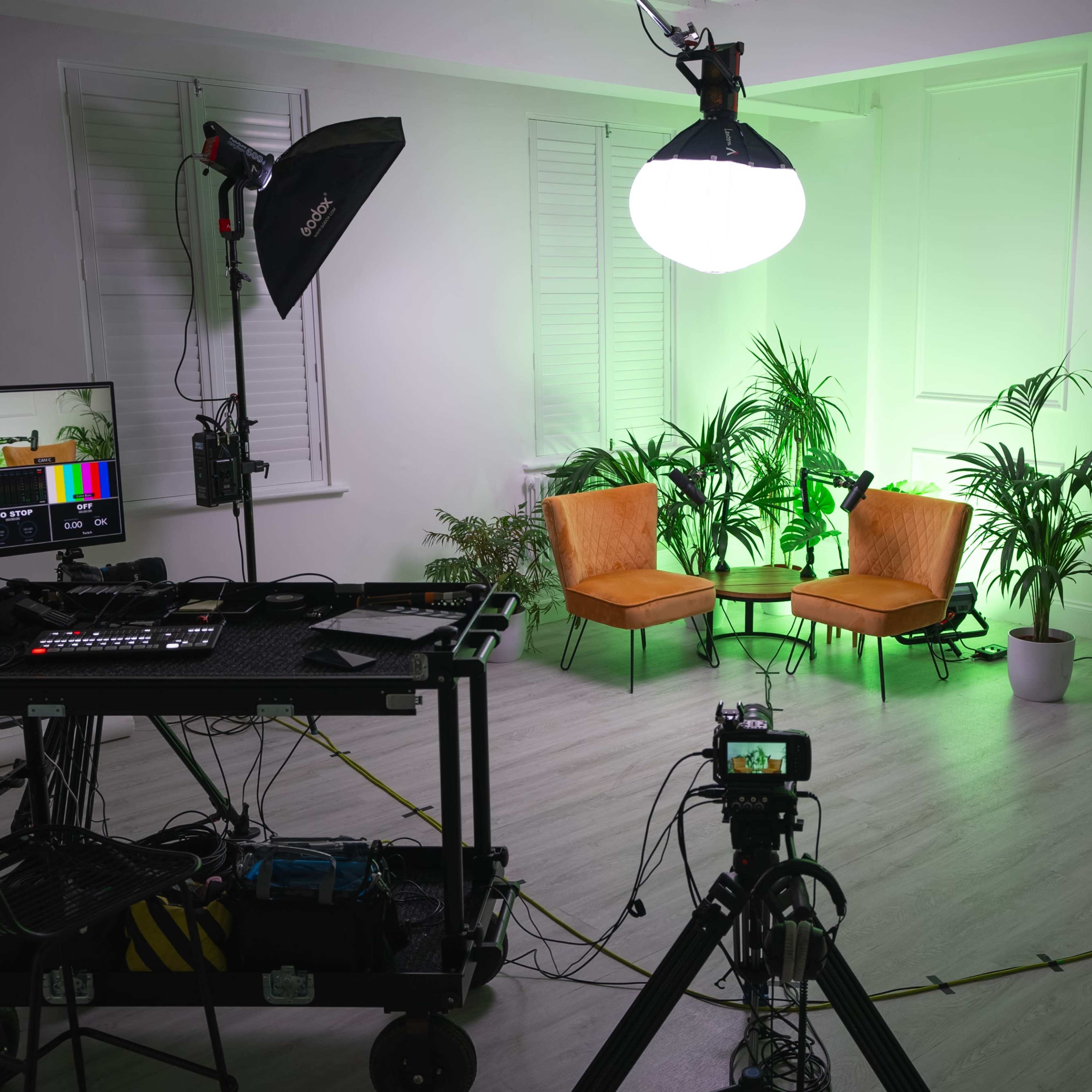 A well-equipped photo studio features two orange chairs, bright lighting, and various pieces of filming equipment arranged around the space.