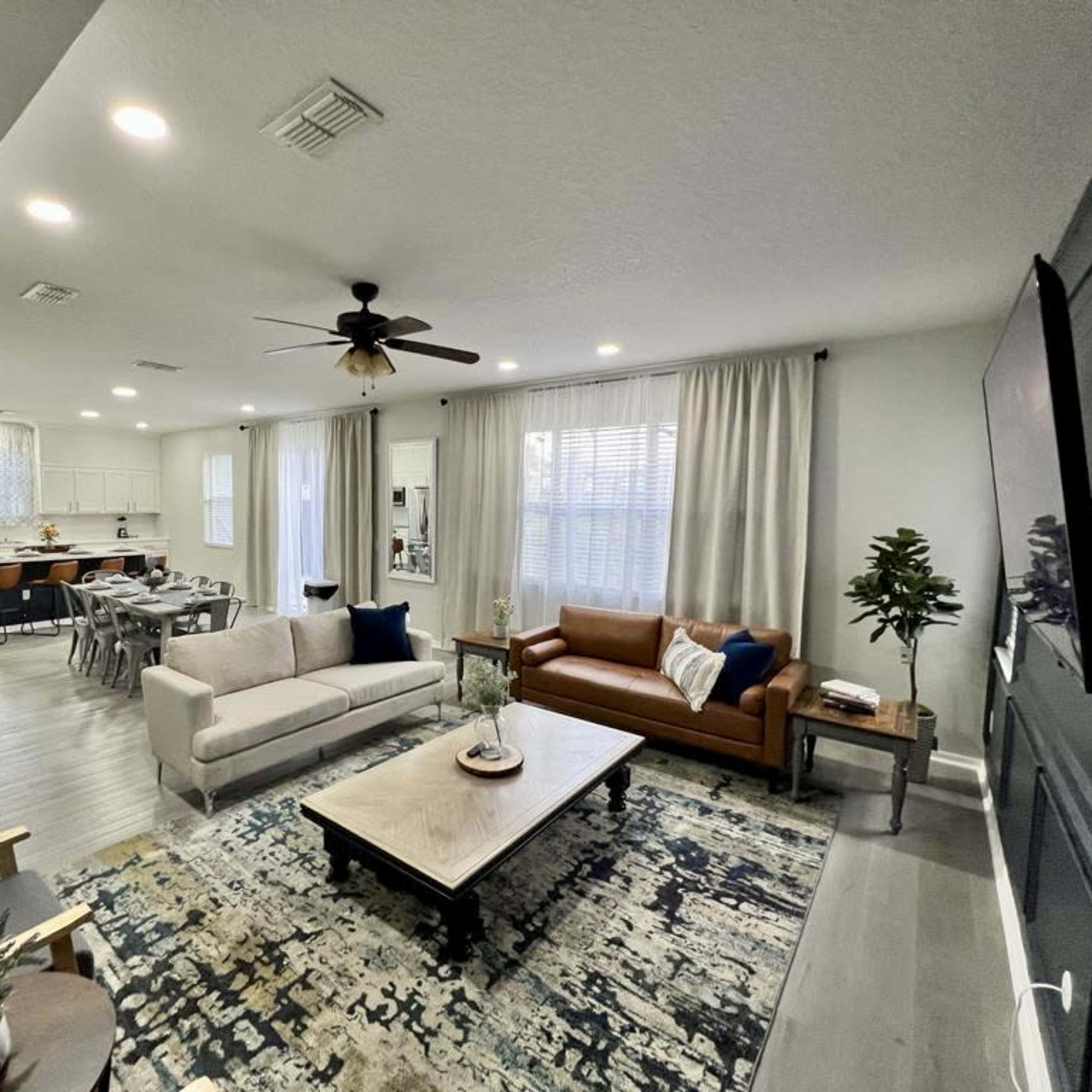A modern living room with a light-colored couch, a brown leather sofa, a coffee table, and a view of an open kitchen area in the background.