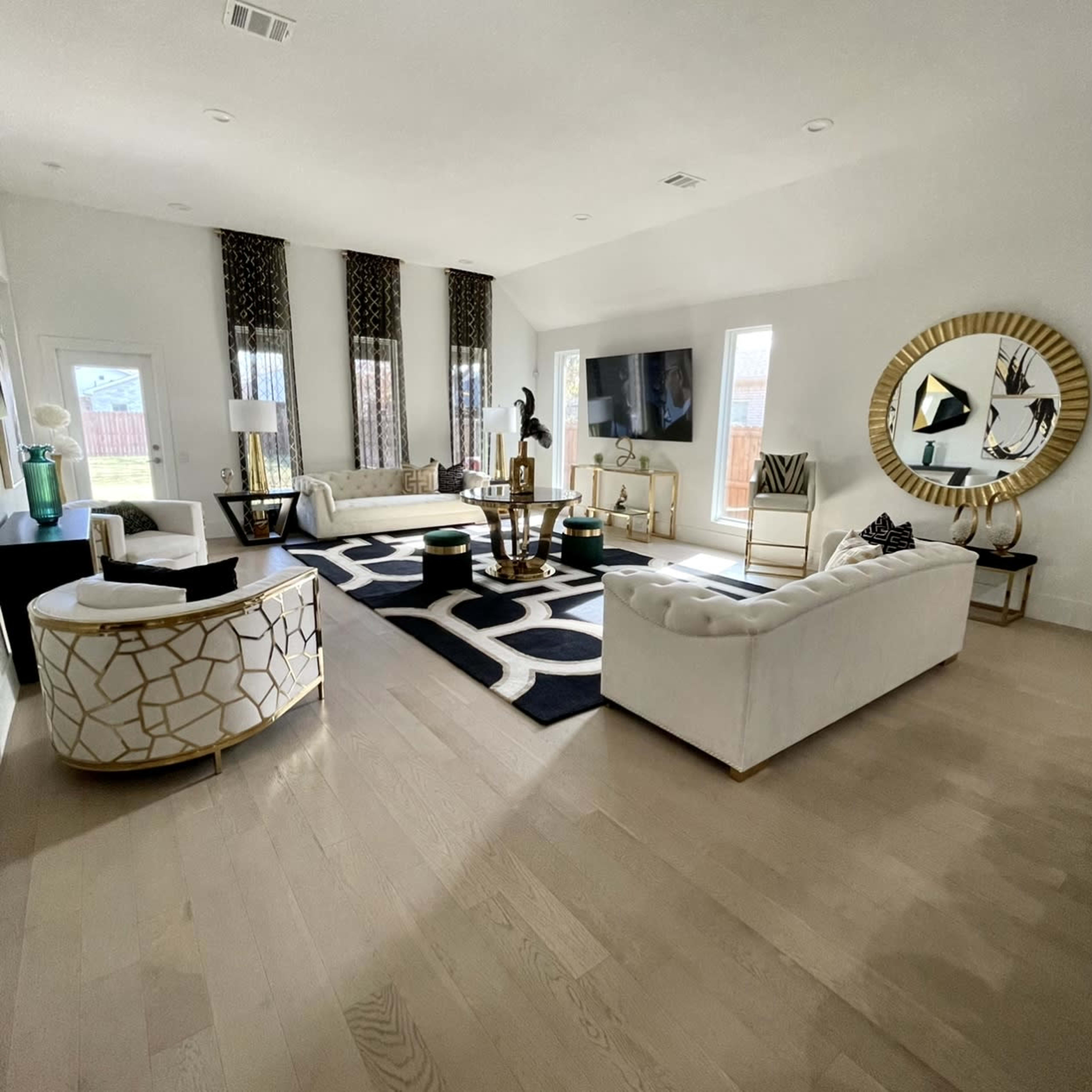 A spacious living room featuring white sofas, a decorative rug, a large wall-mounted television, and stylish furnishings with gold accents.