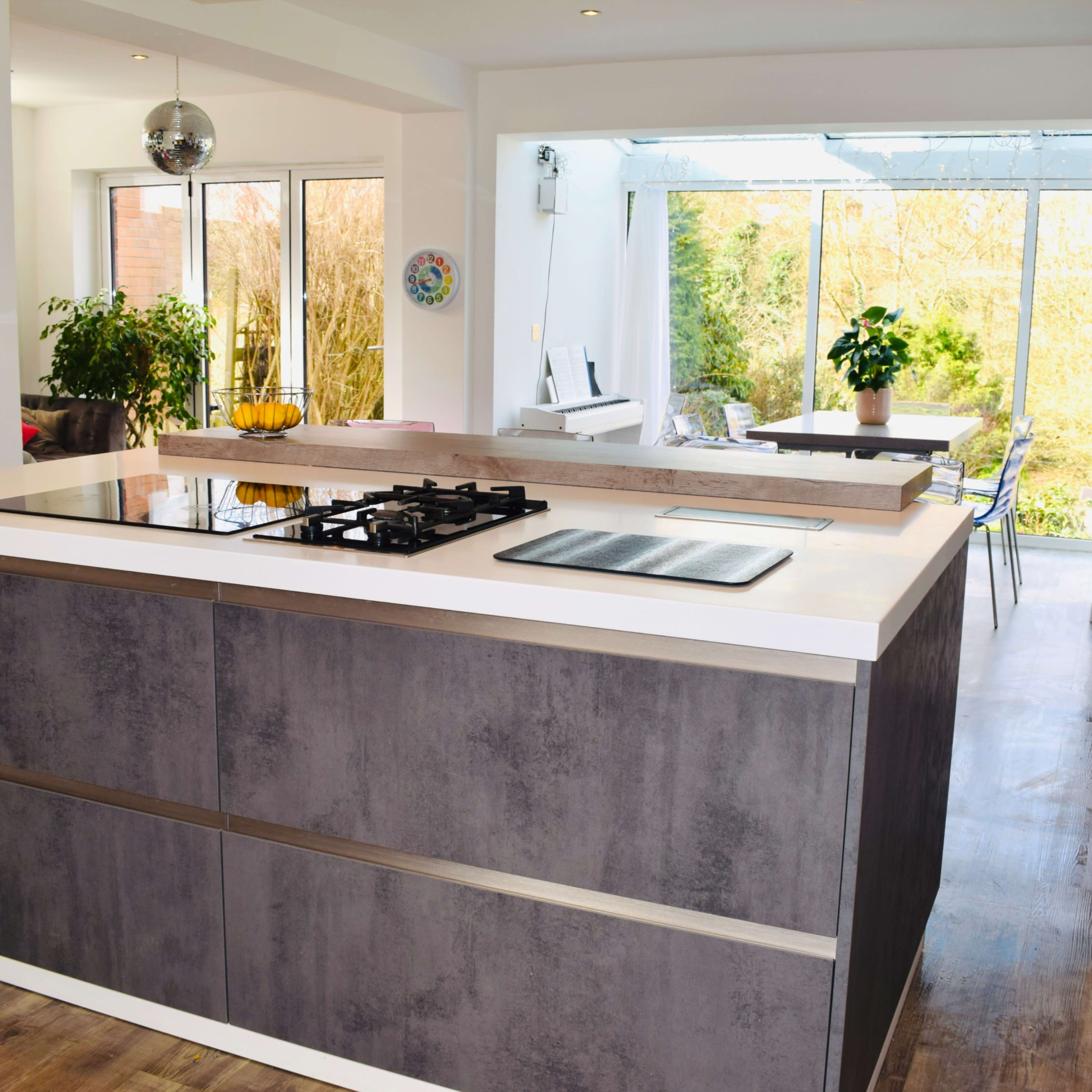 A modern kitchen with a central island featuring a built-in stovetop, surrounded by large windows that overlook a garden.