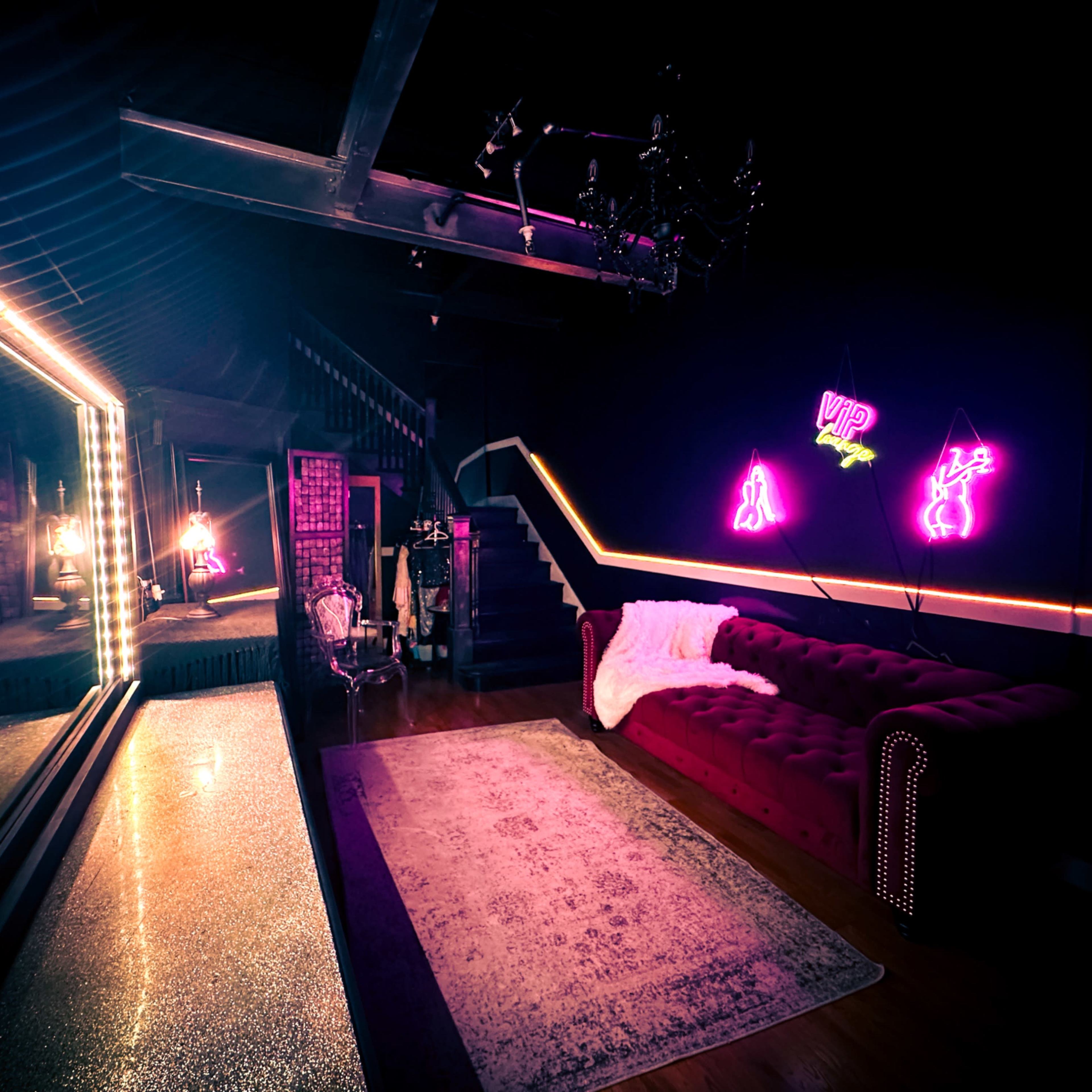 A dimly lit room with a plush red couch, a large mirror, and neon signs on the wall.