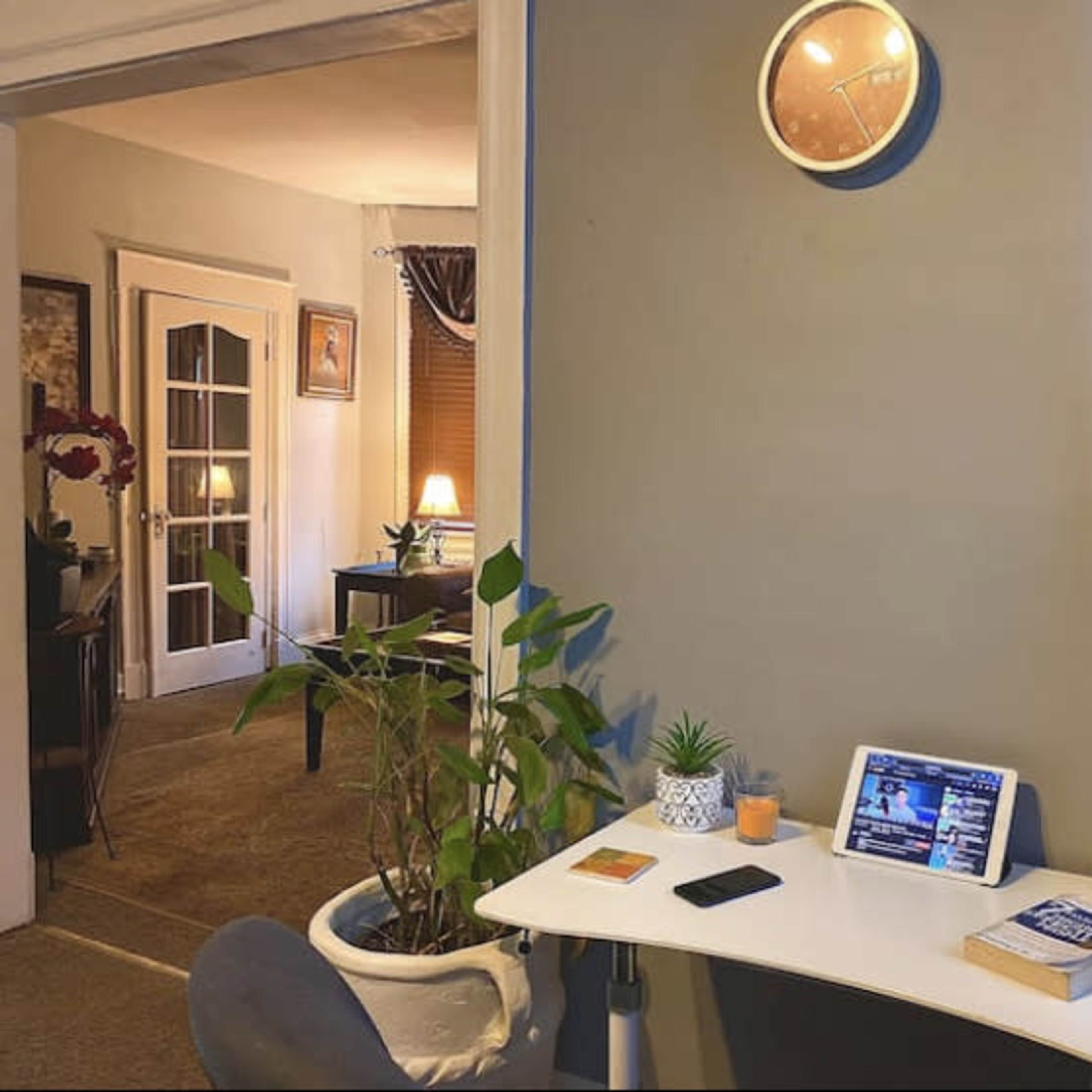 A small table with a tablet, a phone, and houseplants is positioned against a wall in a room that has a doorway leading to another area.