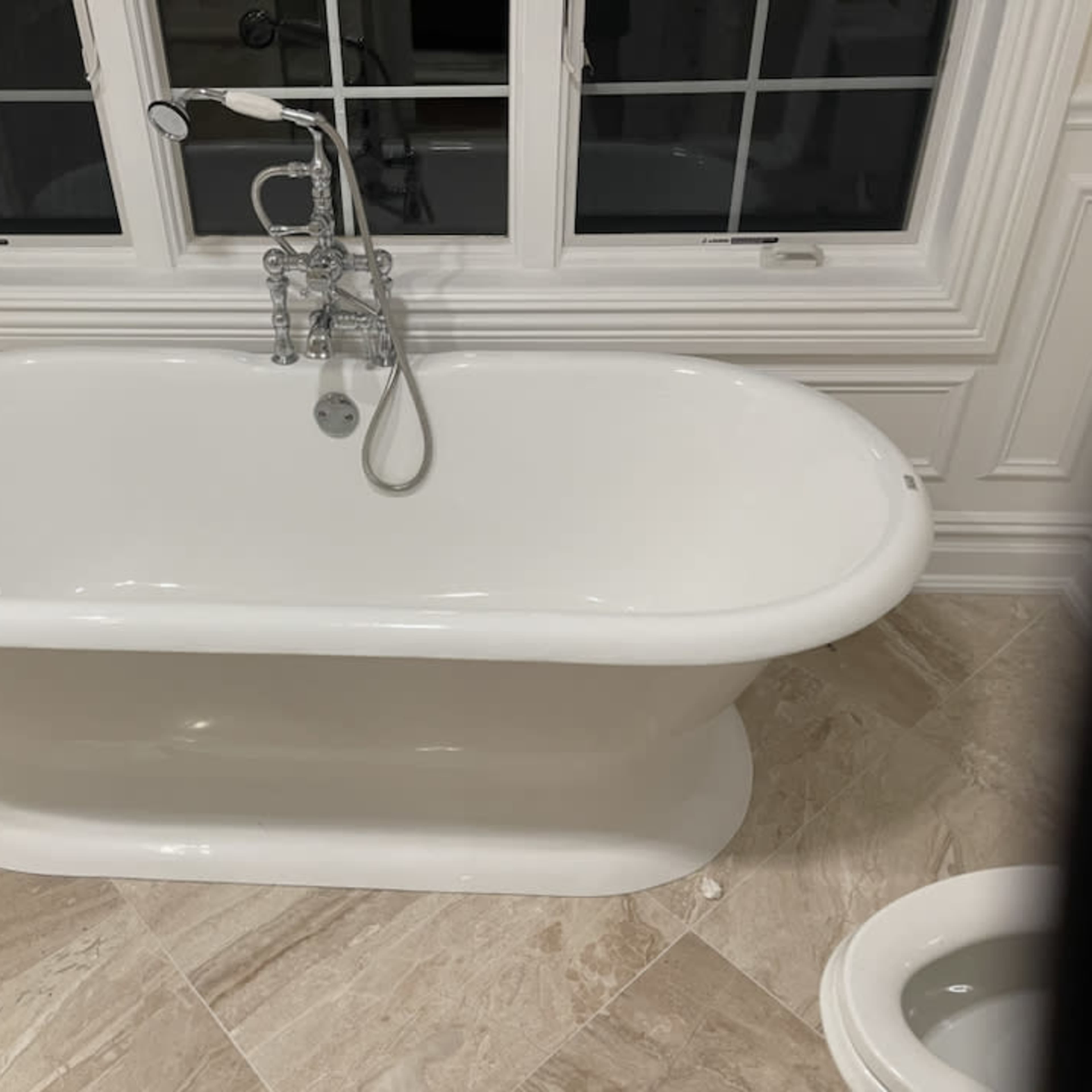 A white freestanding bathtub next to a toilet, with a window providing natural light in the background.