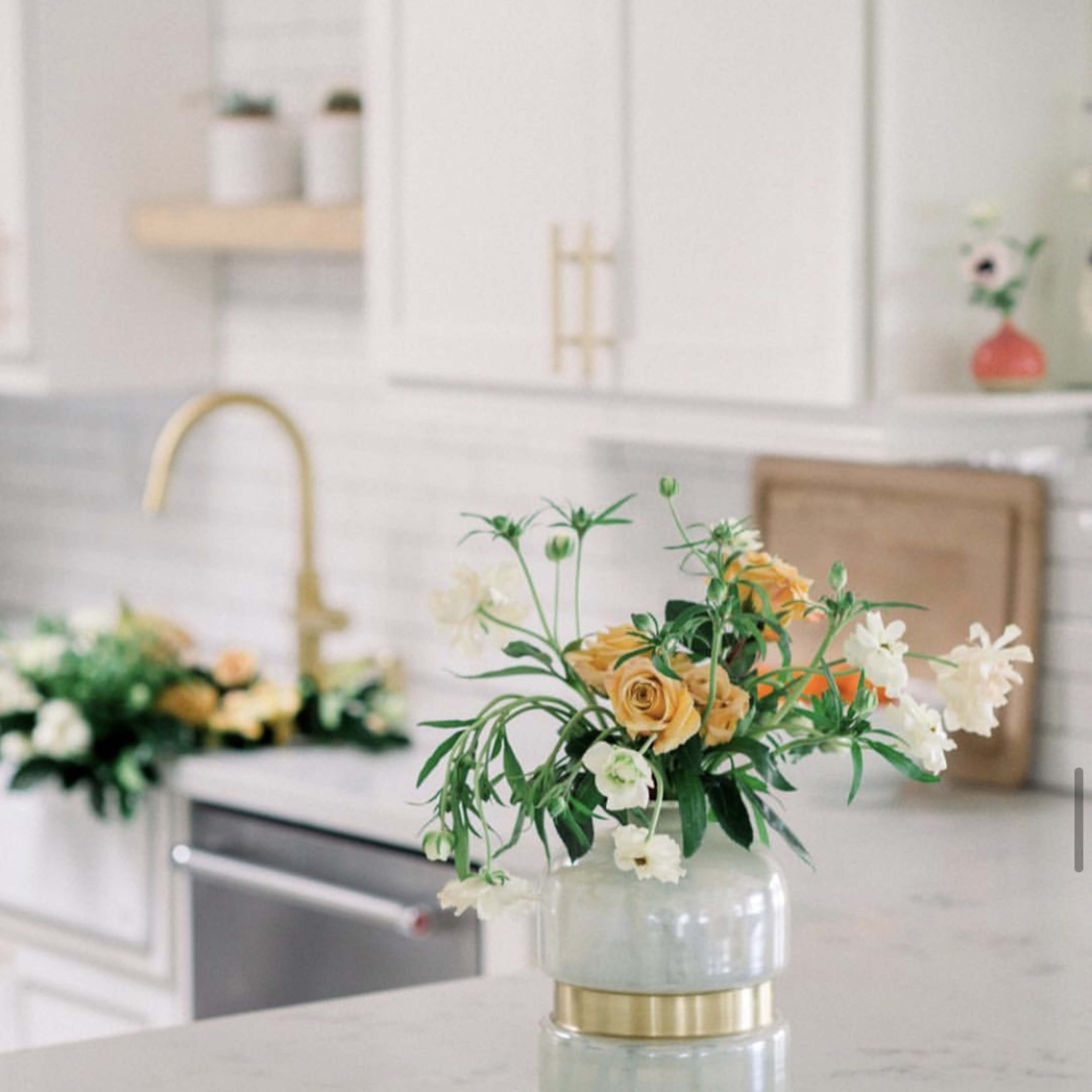 A glass vase filled with orange roses and white flowers sits on a marble countertop in a modern kitchen.