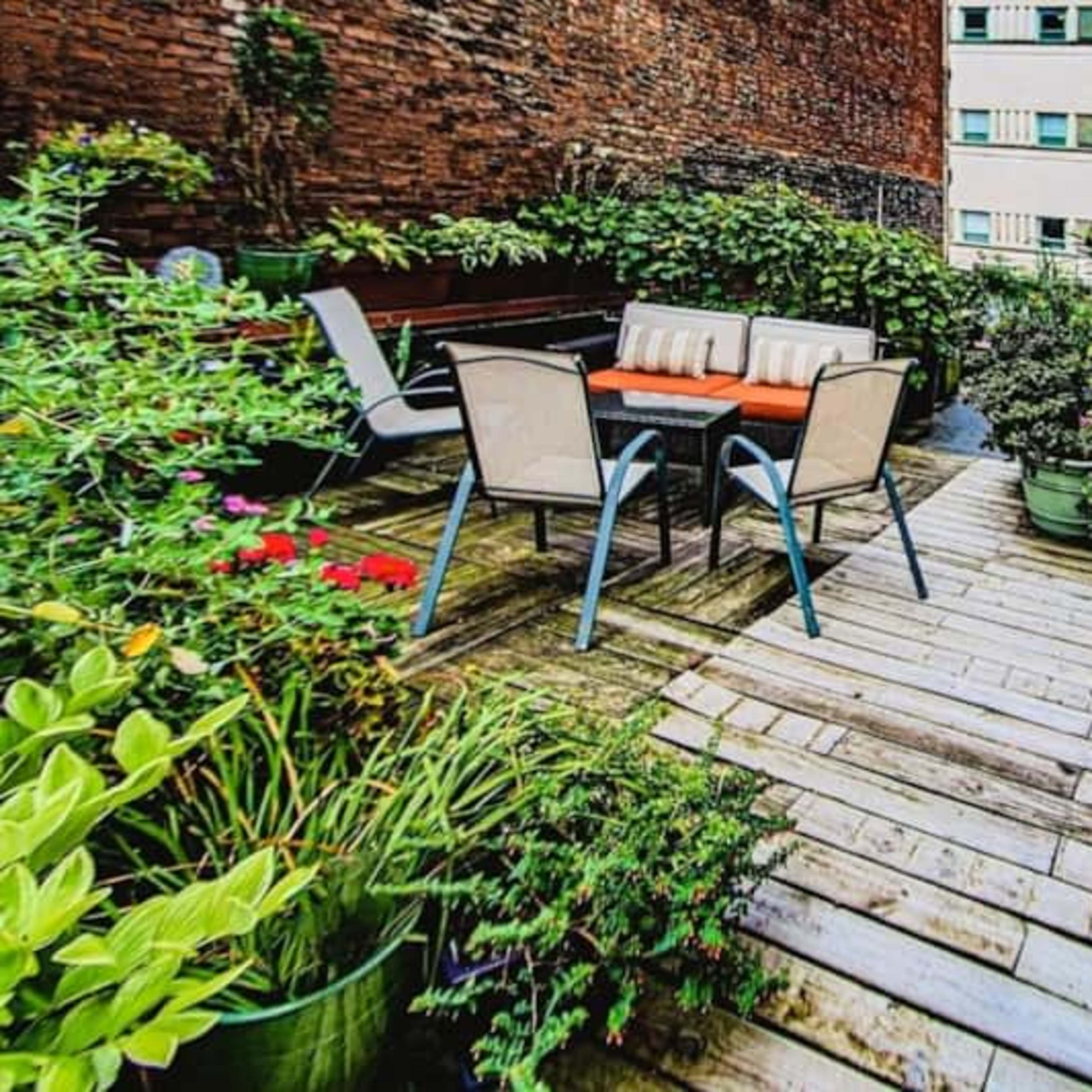 A wooden deck surrounded by vibrant potted plants features a dining table and chairs.