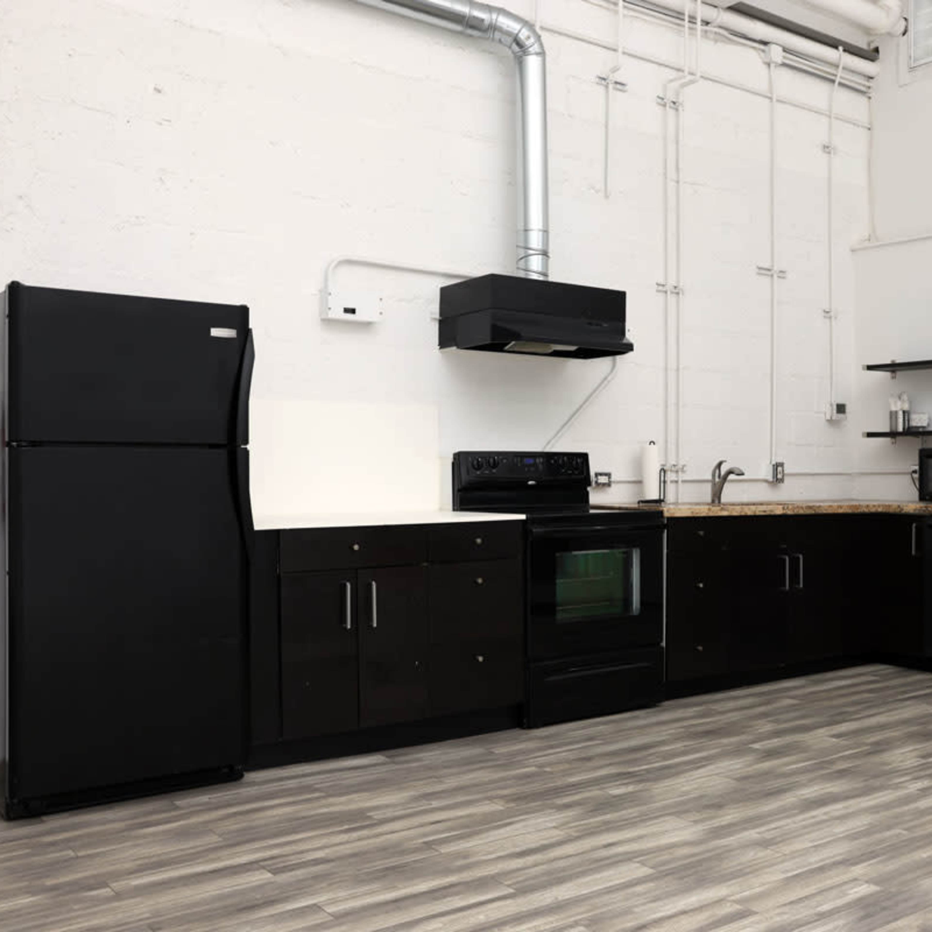 A modern kitchen features black appliances and cabinetry arranged along a textured white wall with wood-like flooring.