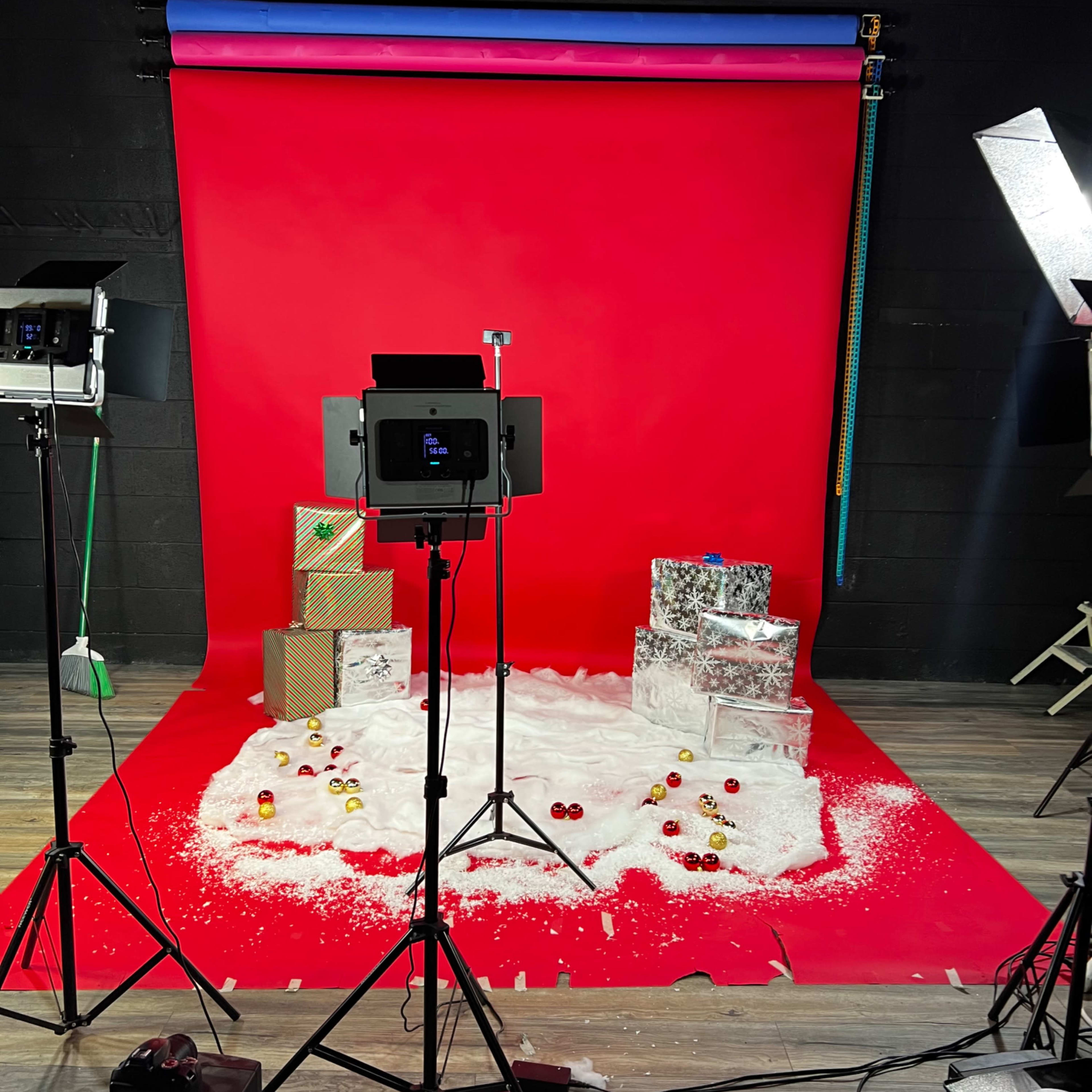 A photography studio set up with red backdrops, decorated gift boxes, and artificial snow on the floor.