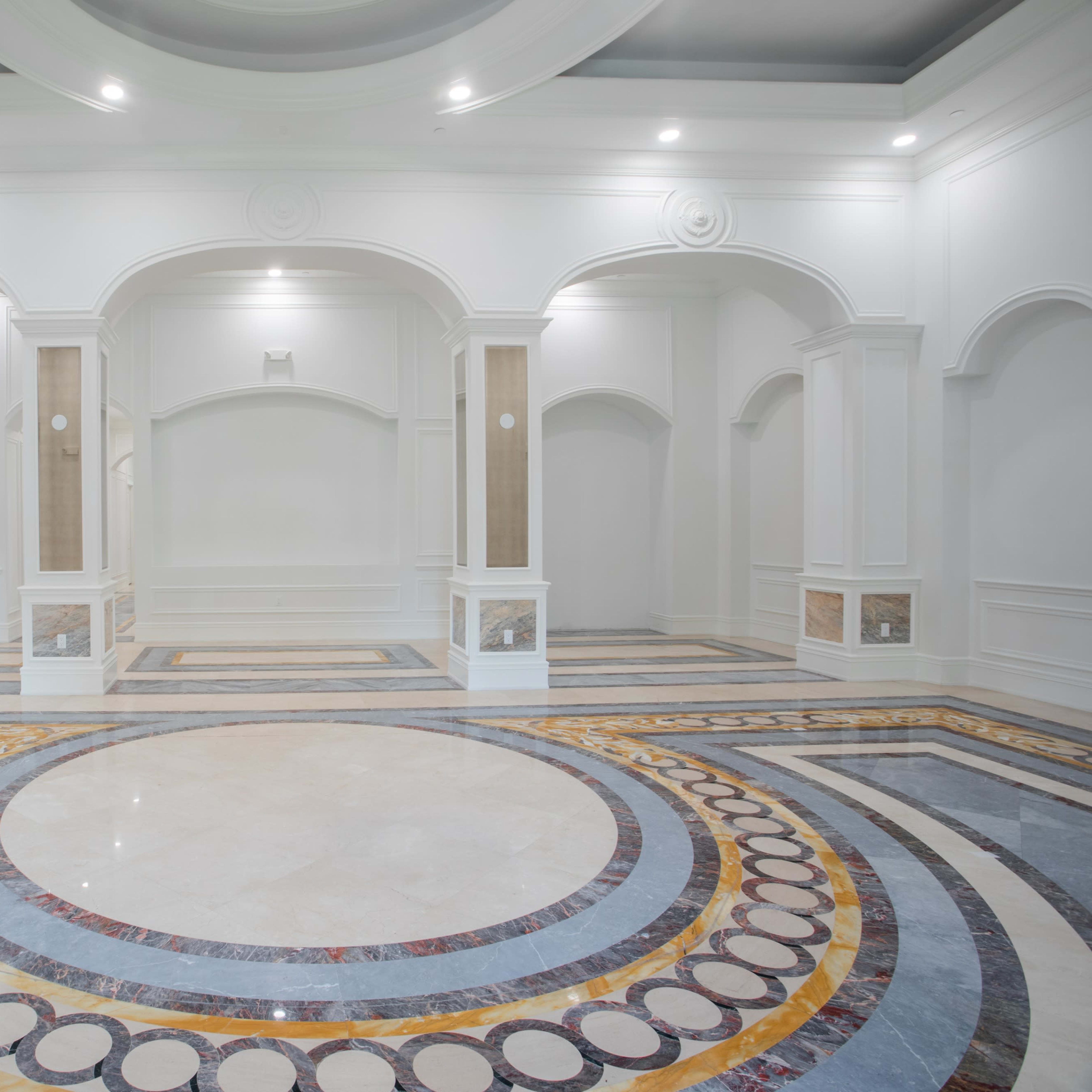 A spacious, elegantly designed room with a circular marble floor pattern and arched architectural elements.