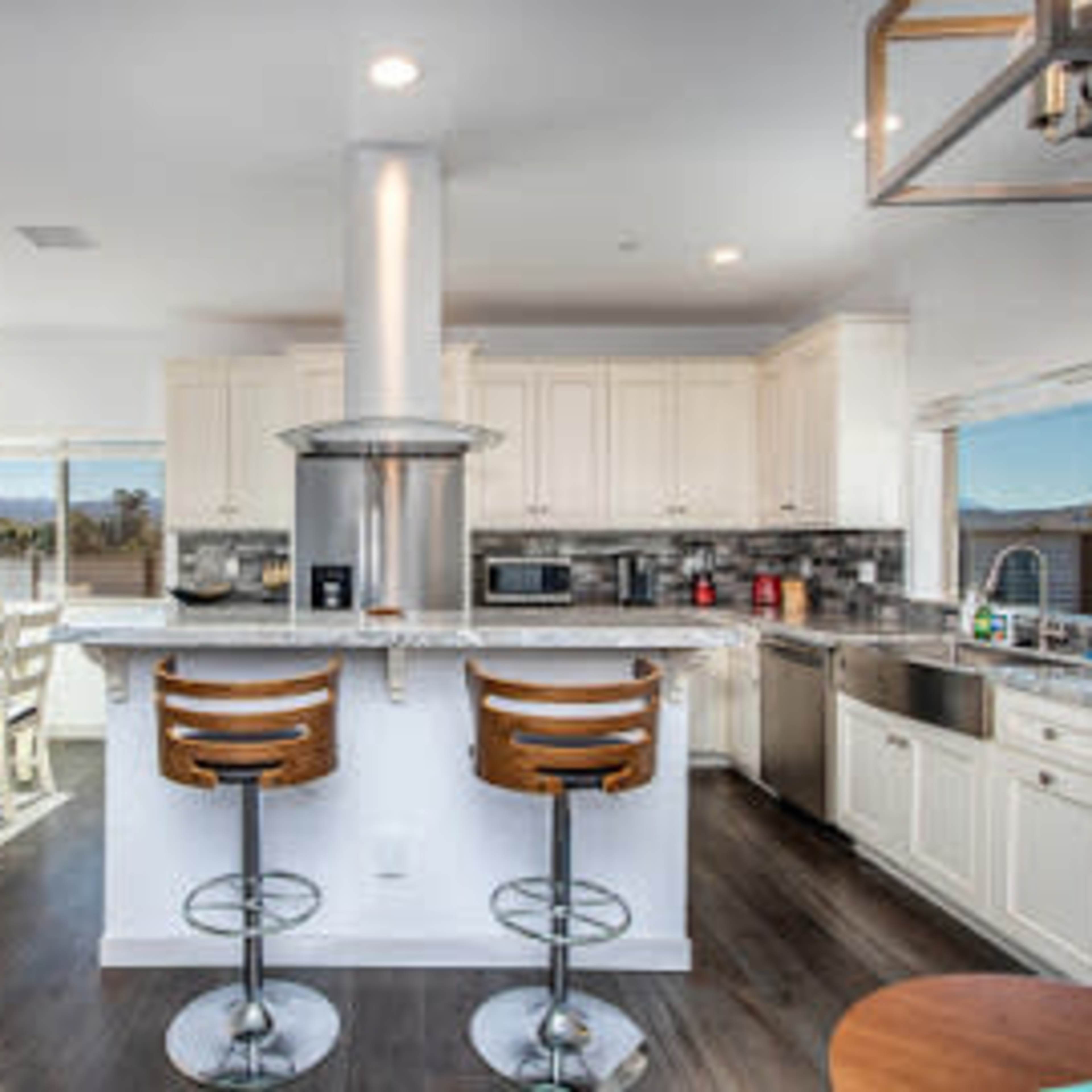 A modern kitchen features white cabinets, stainless steel appliances, and a central island with two wooden barstools.