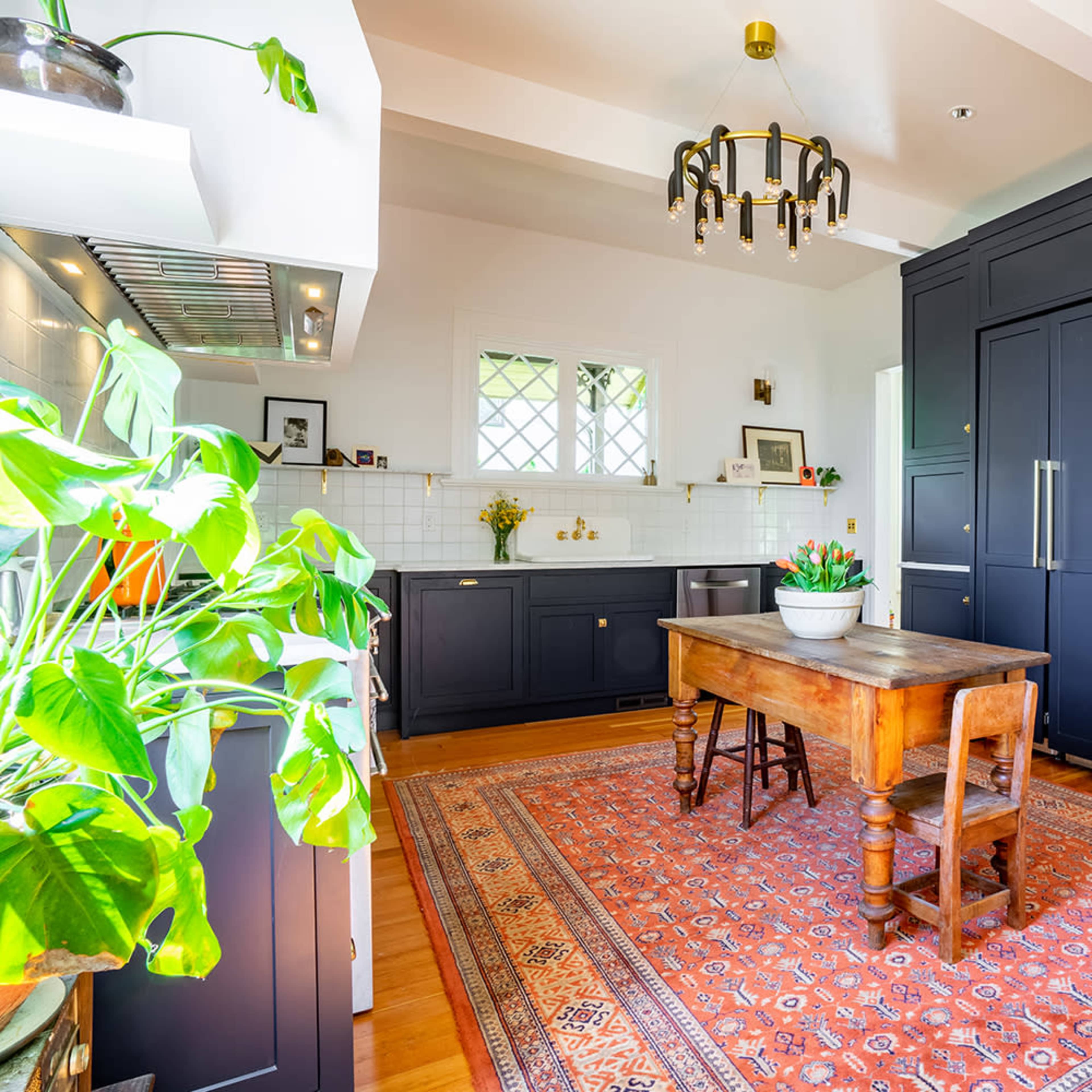 A modern kitchen features dark cabinetry, a wooden dining table surrounded by chairs, and a patterned area rug.