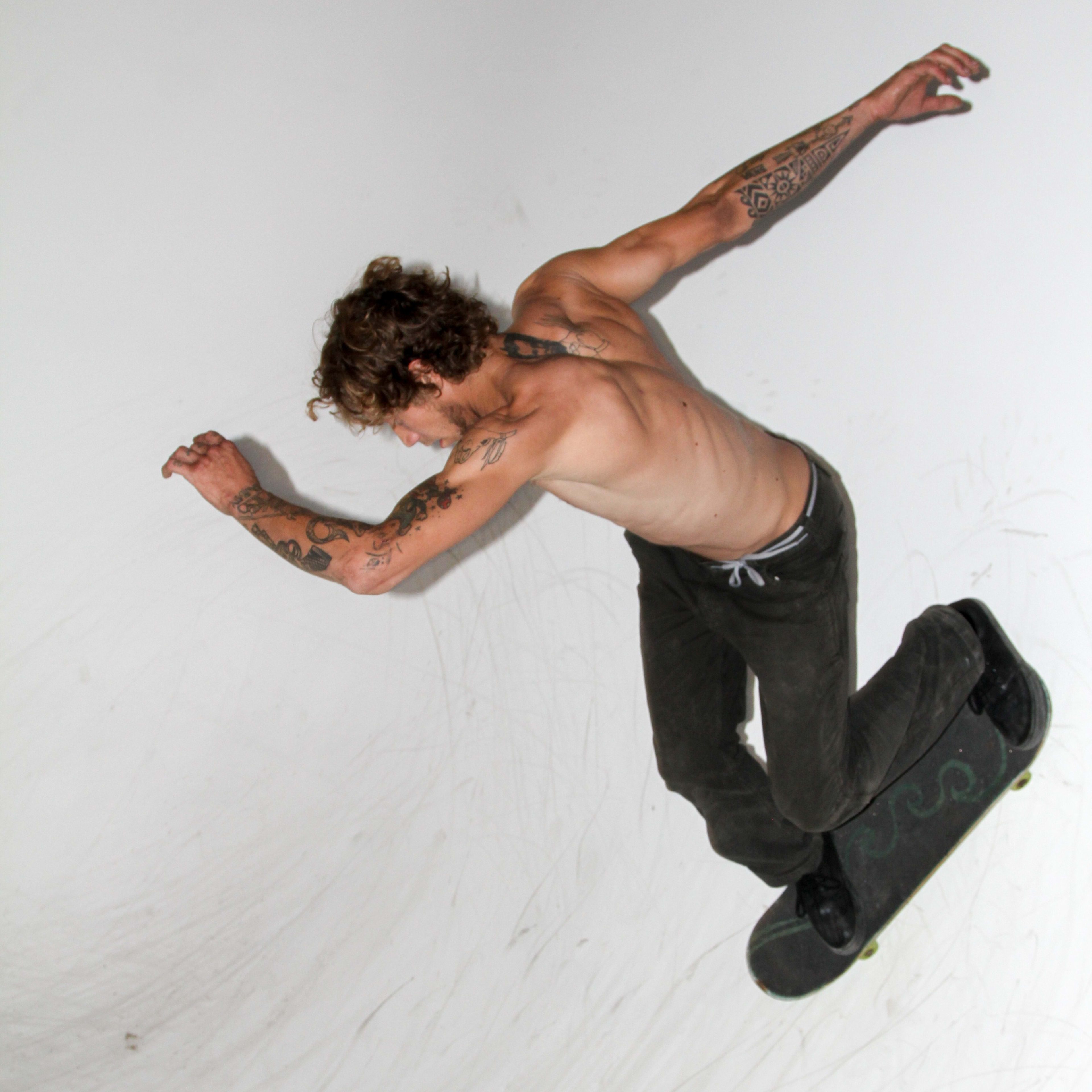 A shirtless skateboarder performs a trick in a half-pipe.
