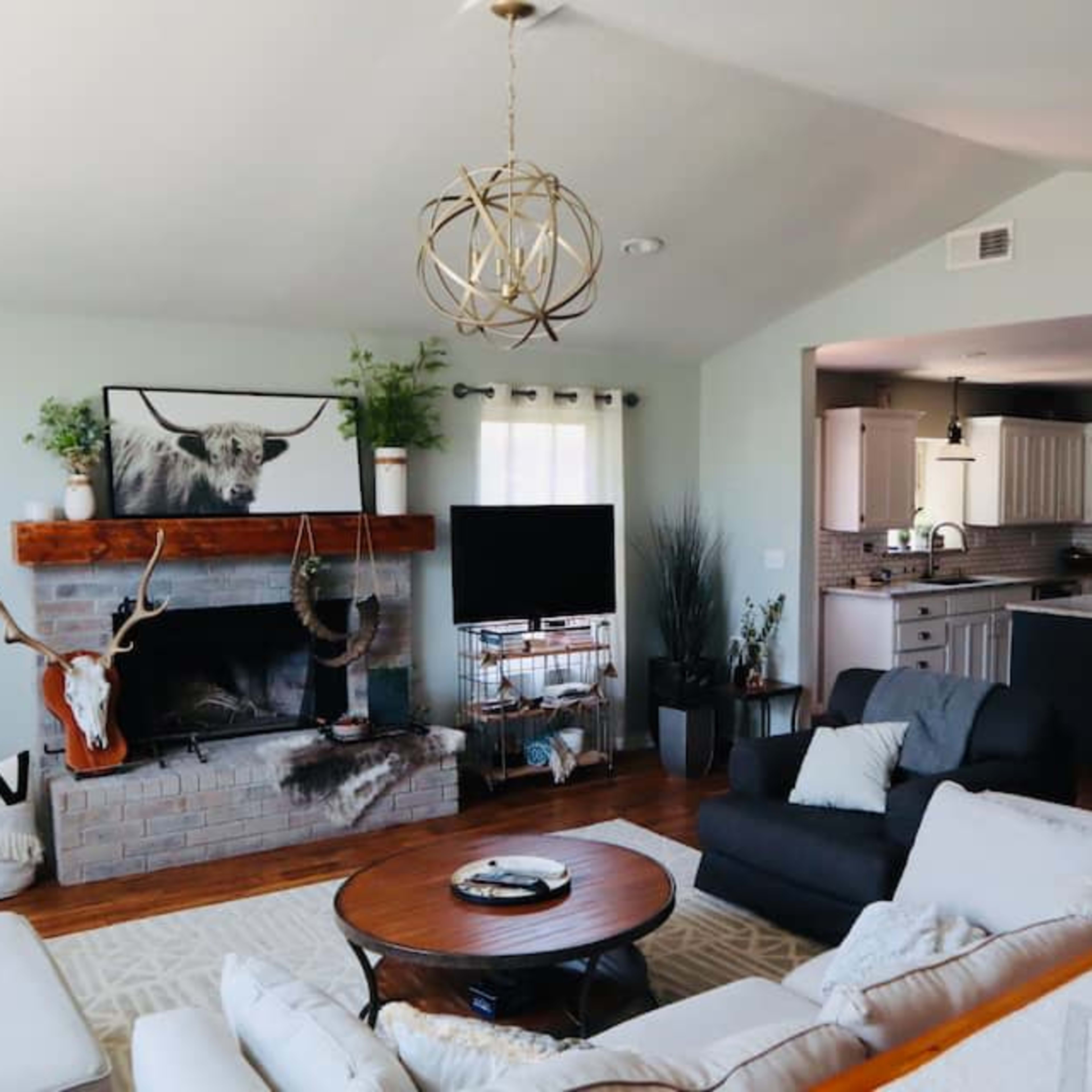 A spacious living room with a rustic fireplace, a television, and a kitchen area visible in the background.