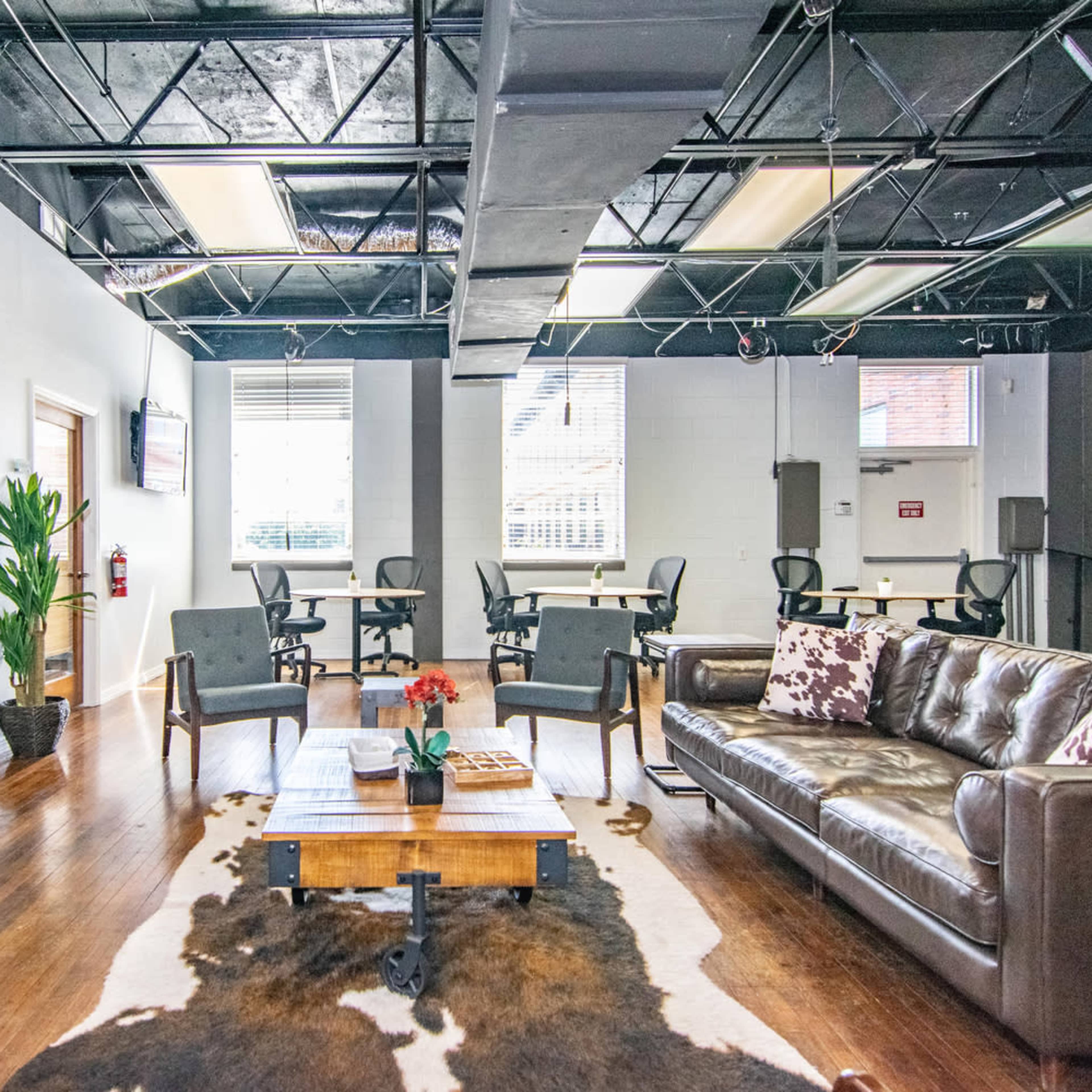 A modern workspace with a lounge area featuring a brown leather sofa, a coffee table, and multiple desks in the background.