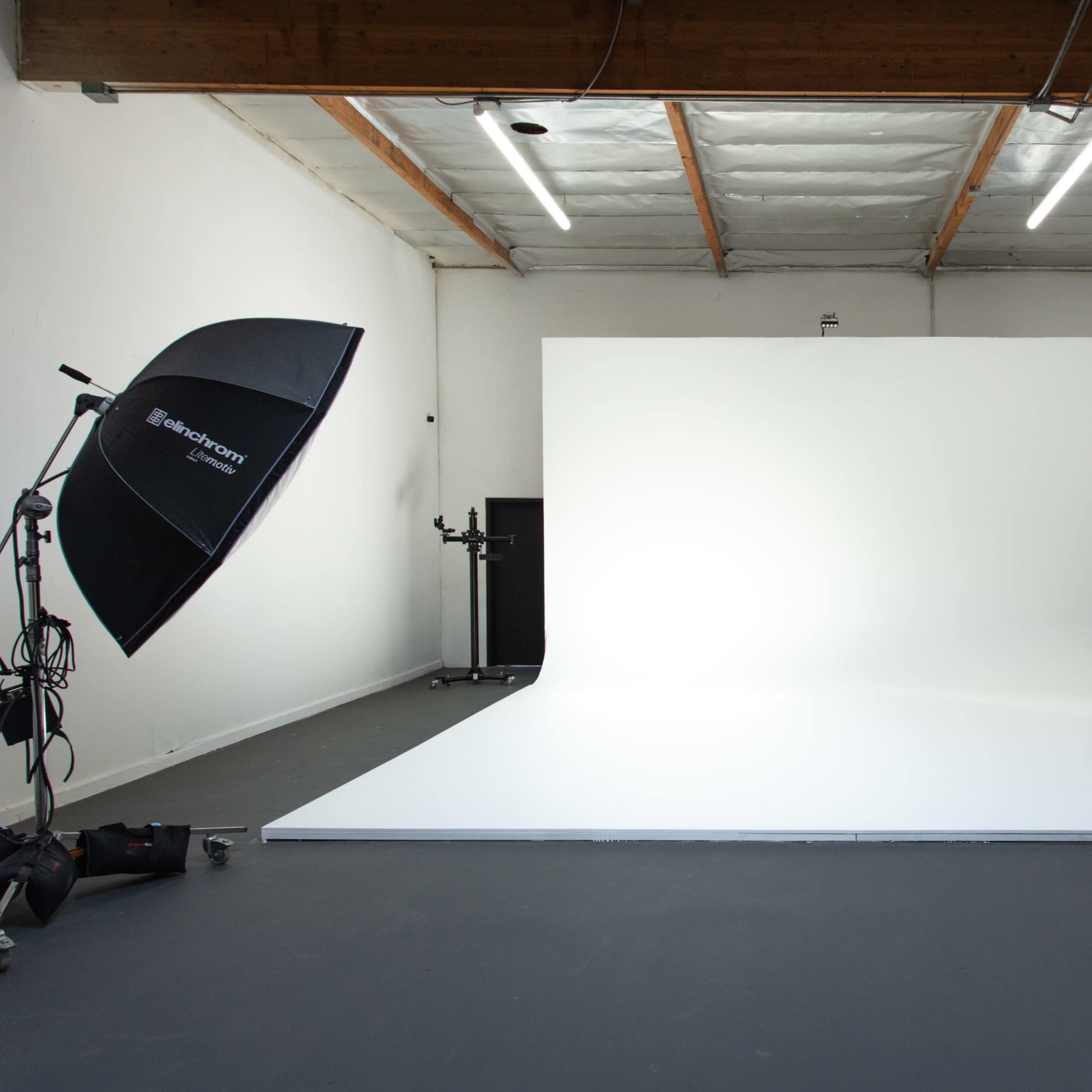 A photography studio featuring a large white backdrop, a softbox light, and a plain floor.