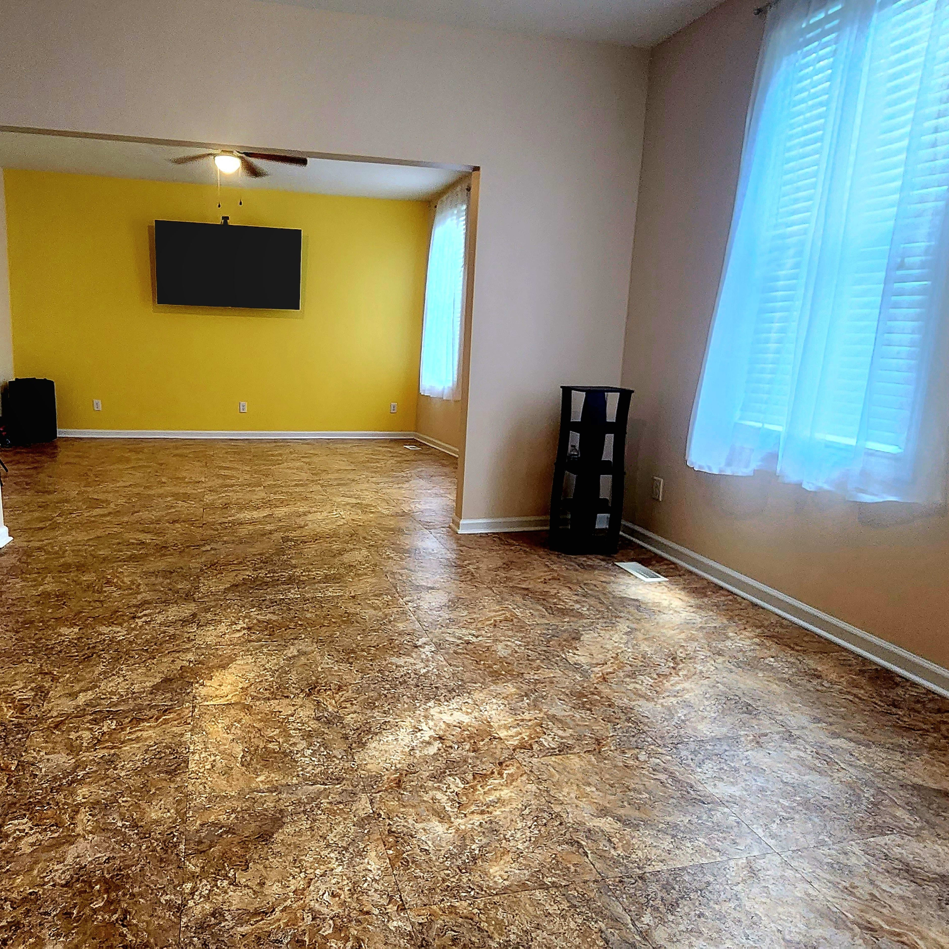 A spacious, open room with light-colored walls, a yellow accent wall, and a TV mounted on the opposite wall.
