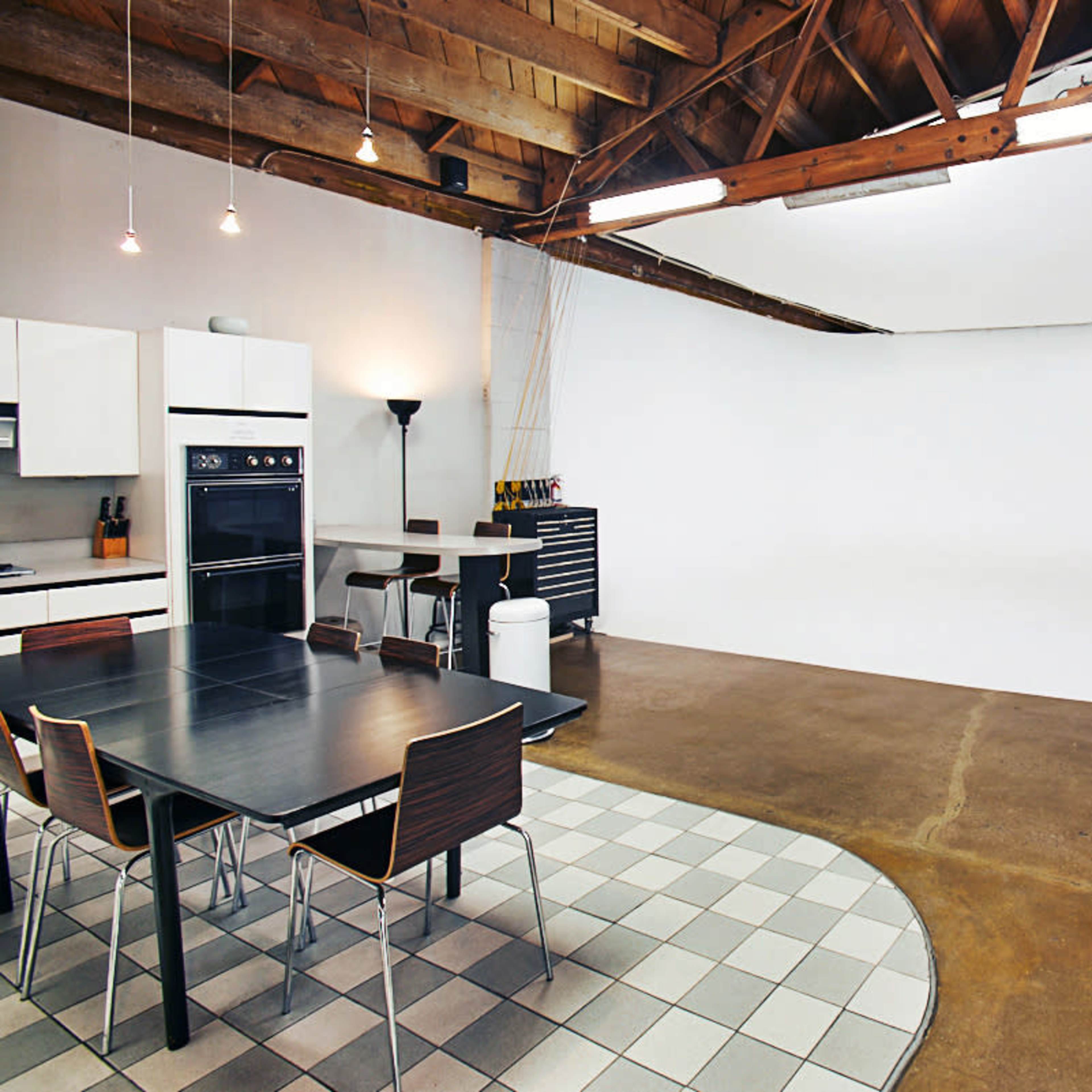 A spacious studio with a kitchen area, dining table, and a large, empty white backdrop.
