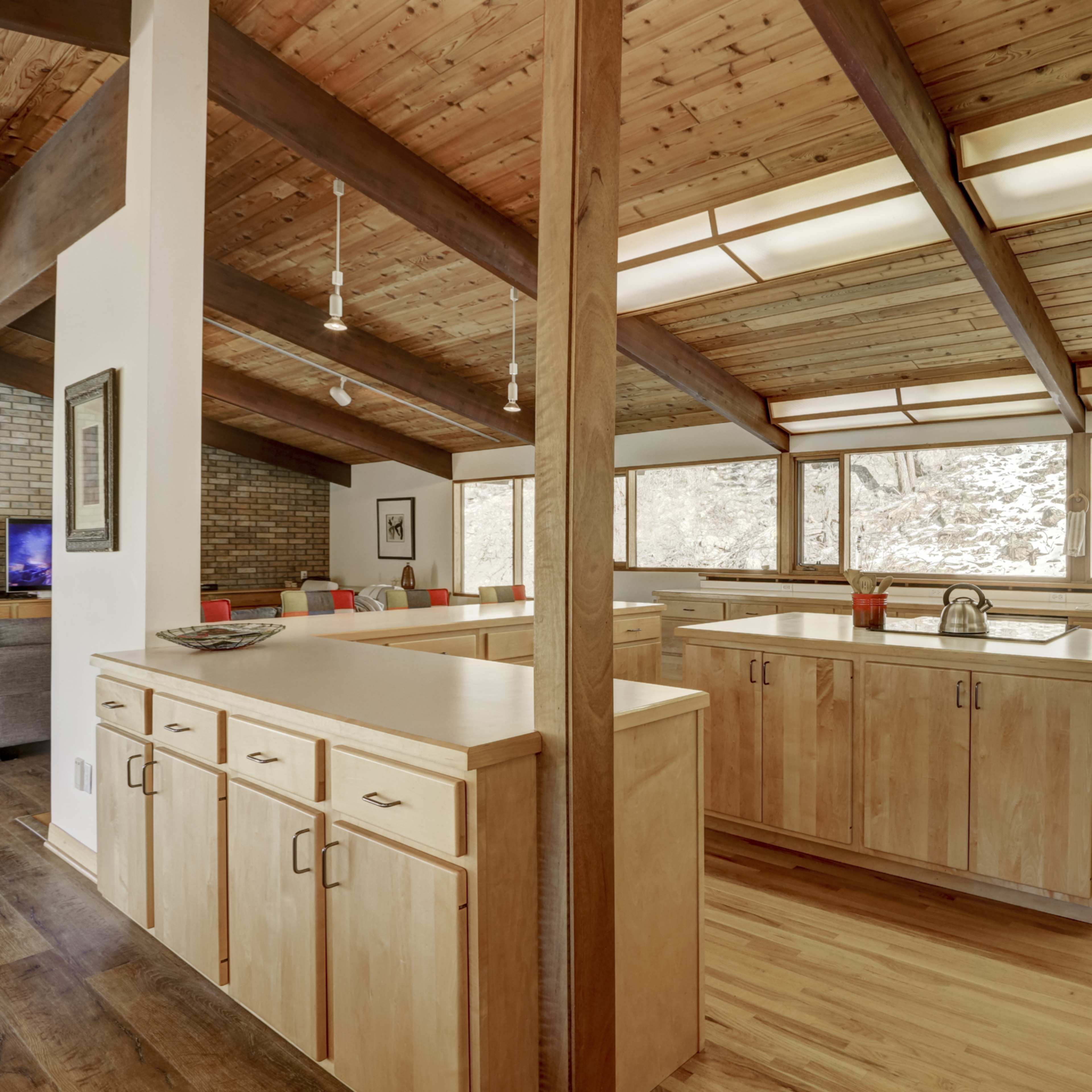A spacious kitchen with wooden cabinetry, marble countertops, and large windows providing natural light.