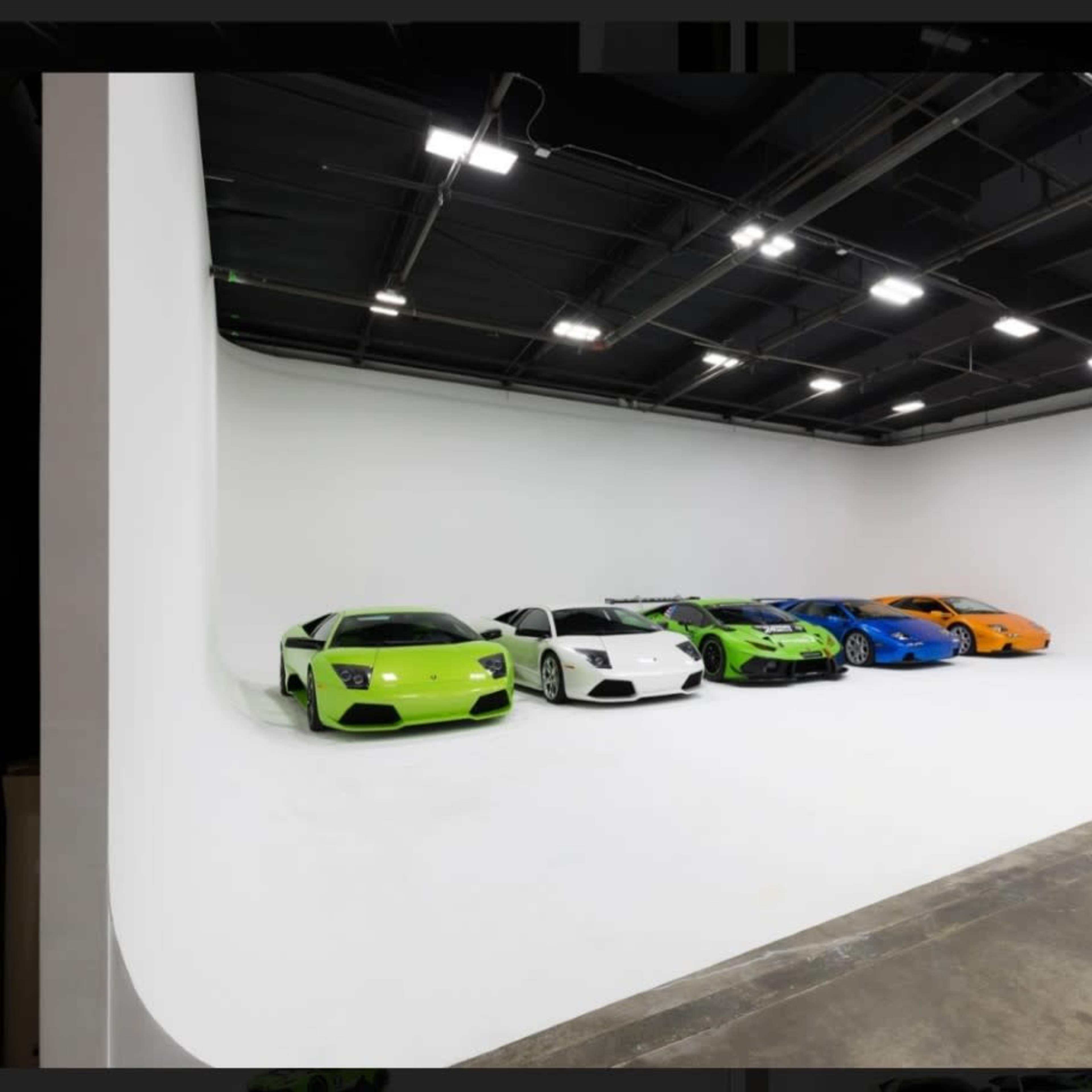 A line of six brightly colored sports cars is displayed against a seamless white backdrop in an indoor studio space.