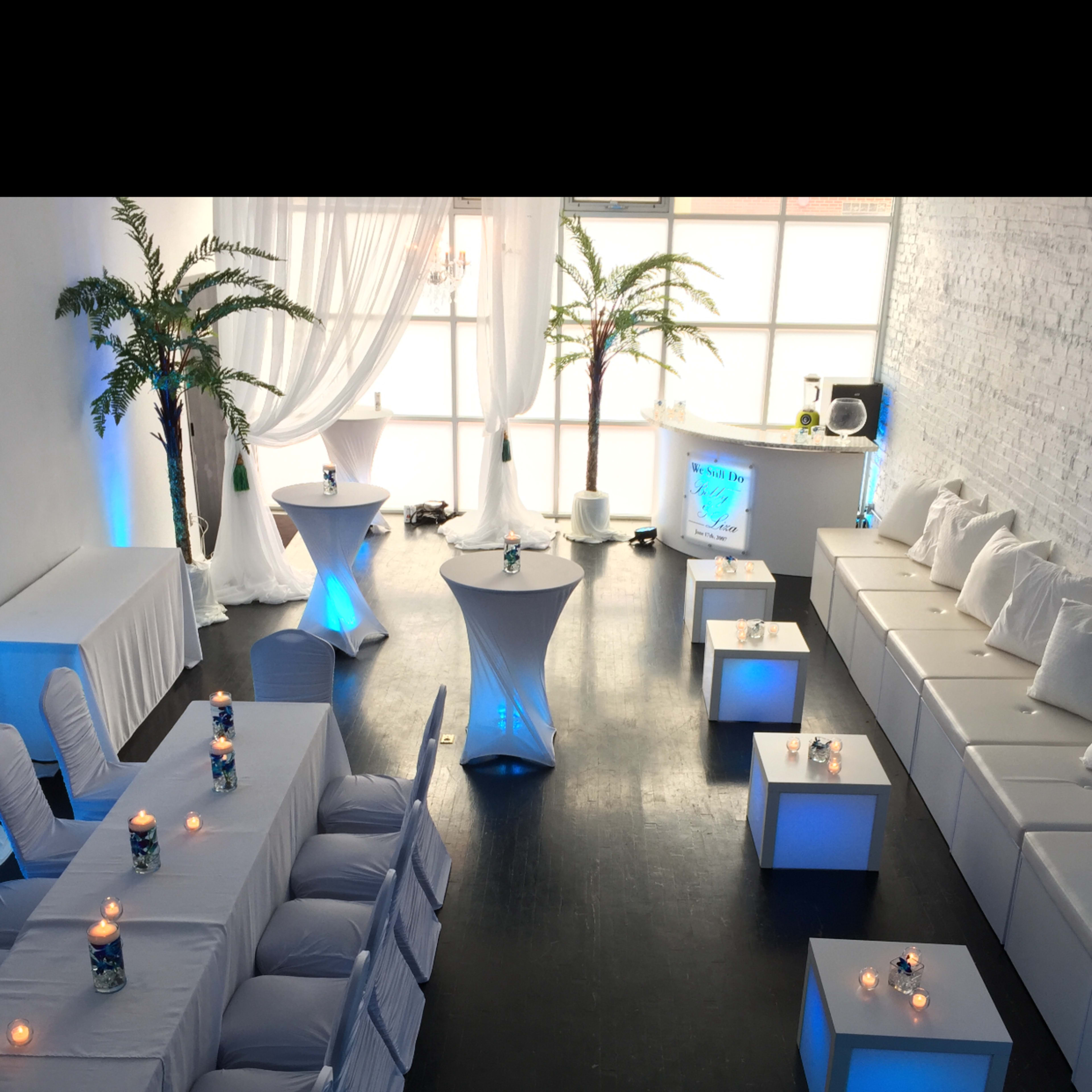 A stylish event space with white furniture and blue lighting, featuring tables set for a gathering.