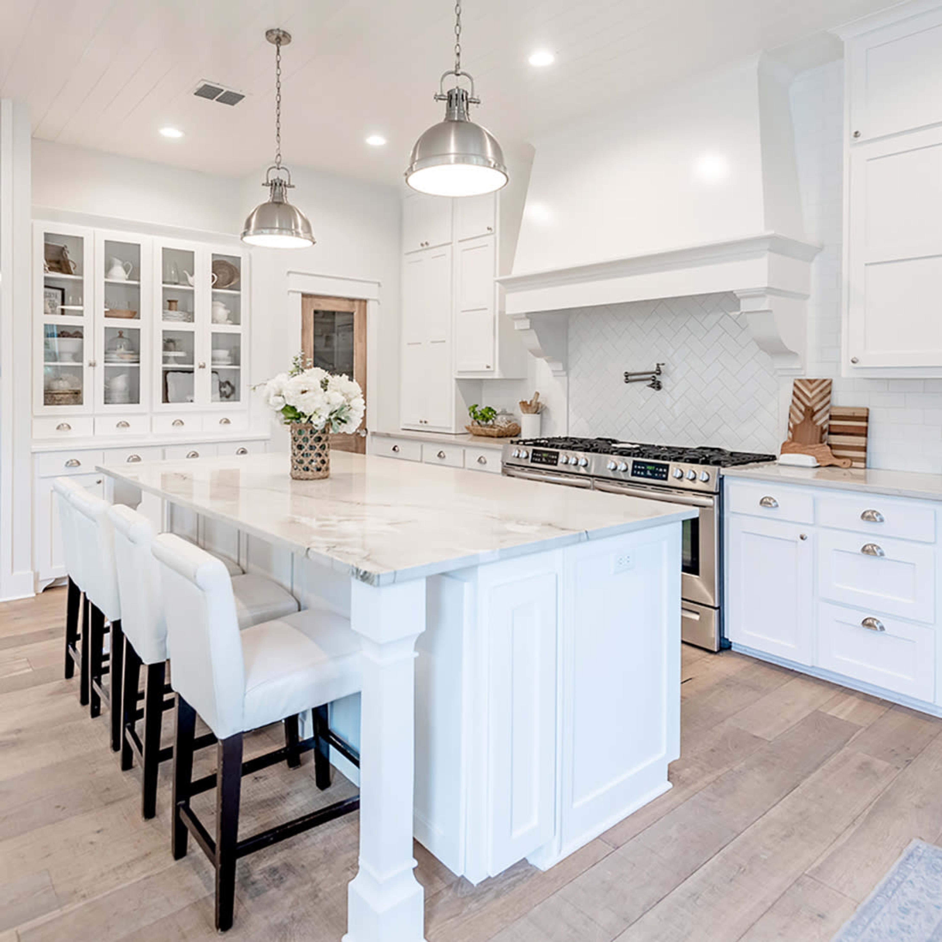 A modern kitchen with white cabinetry, a large marble island with seating for six, and stainless steel appliances.