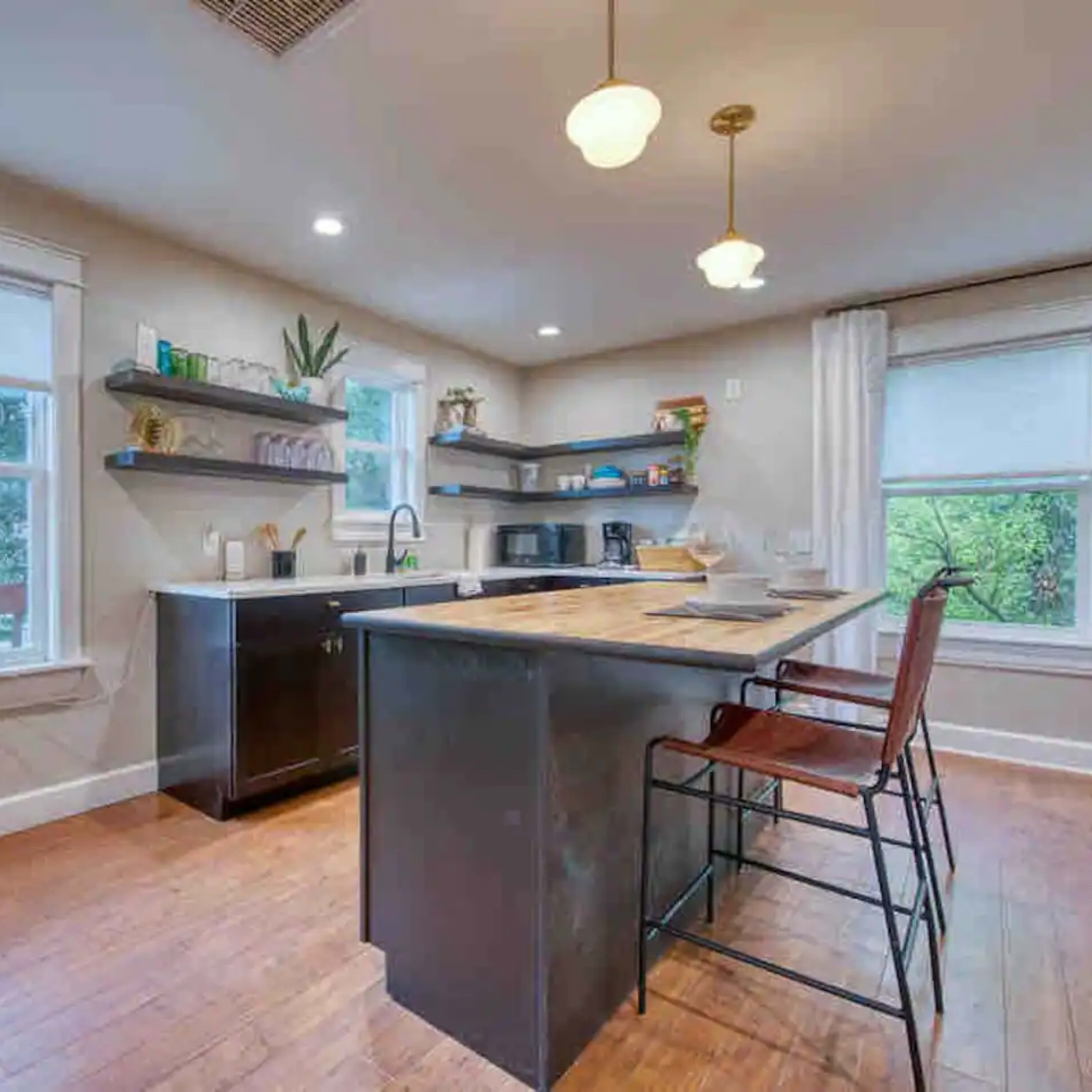 The kitchen features a central island with seating, modern appliances, and shelves displaying plants and kitchenware.