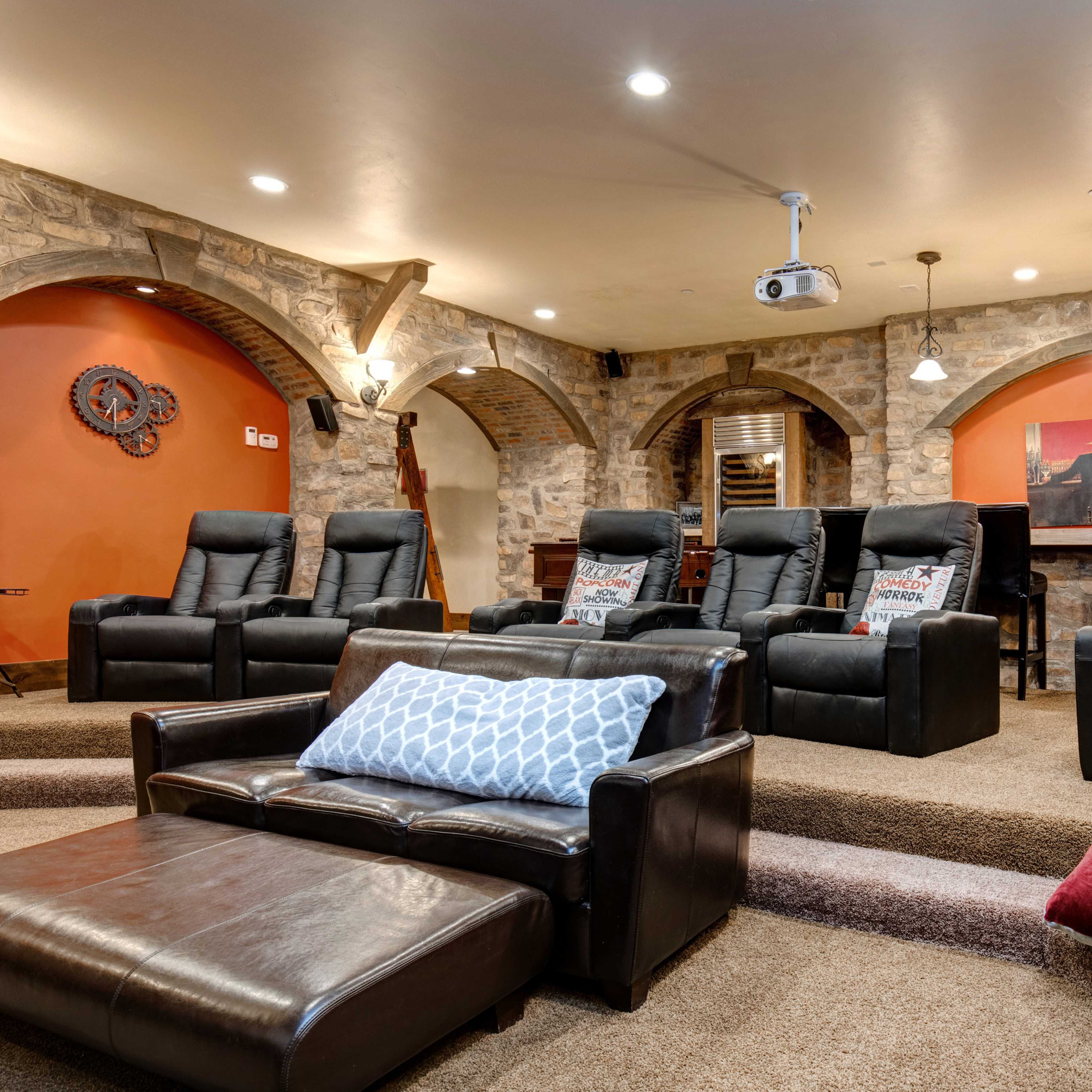 A home theater with stone walls, tiered seating, recliner chairs, and a projector.