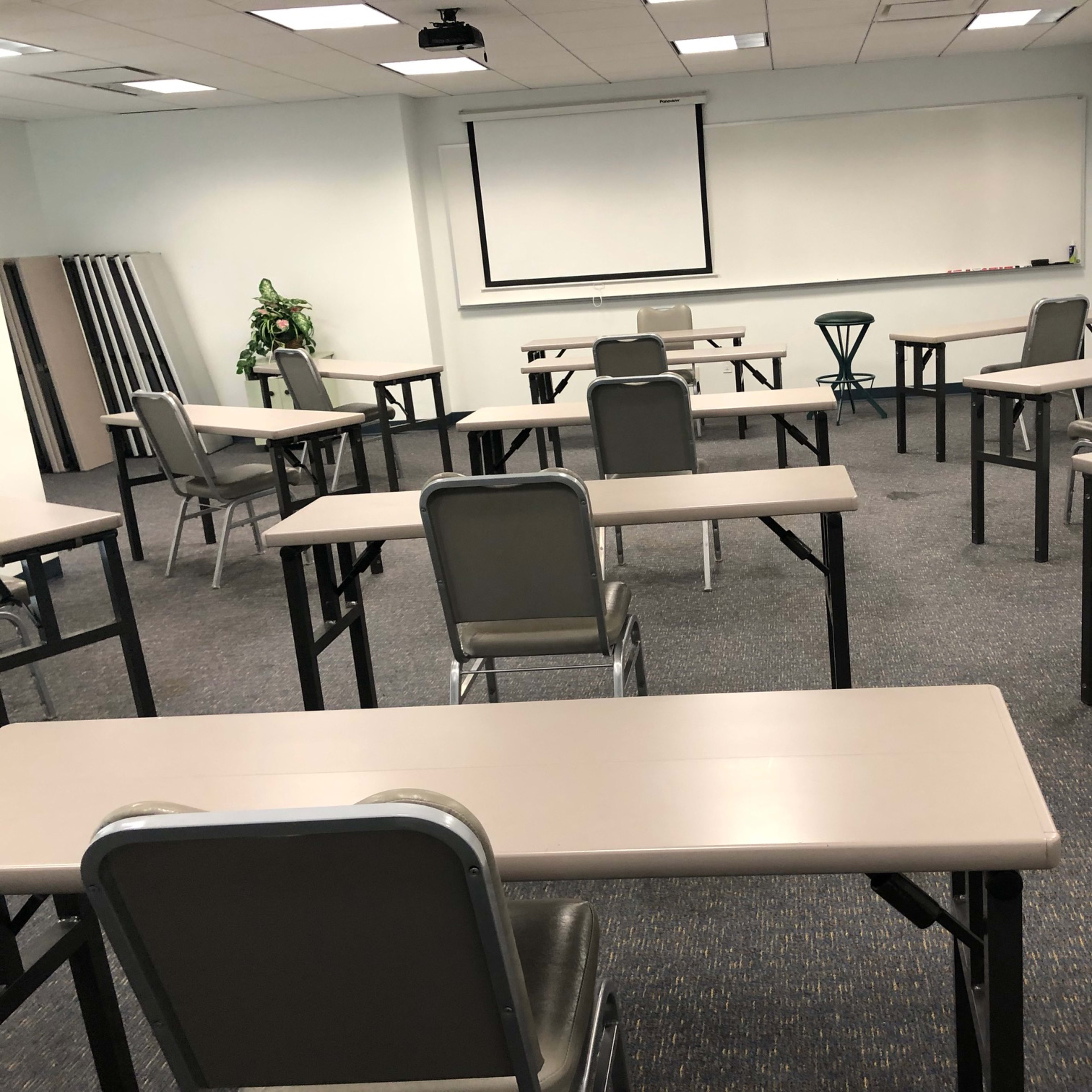 A seminar room features several empty tables and chairs arranged neatly, with a projector screen at the front.