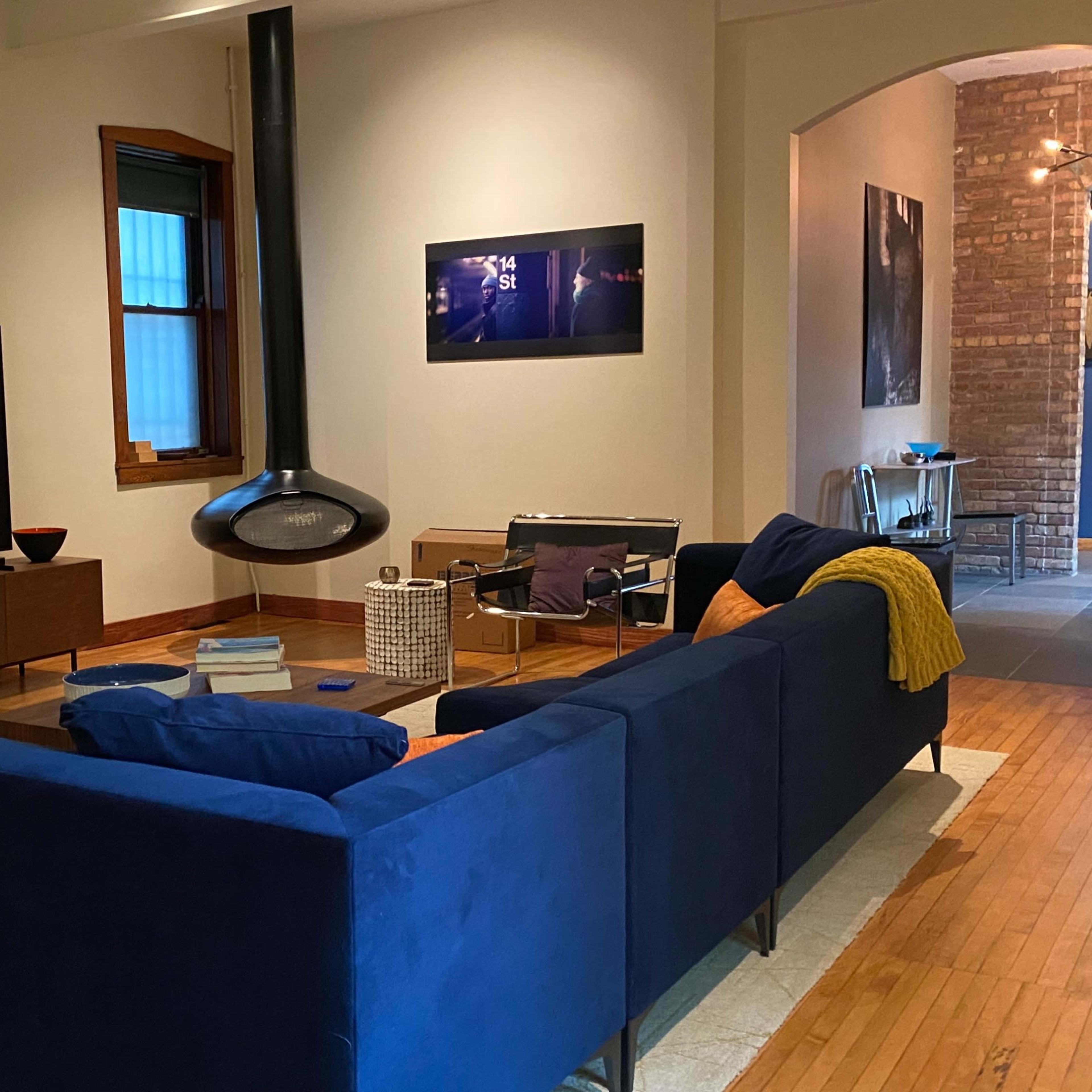 A modern living room with a blue sectional sofa, a large television on a media console, and an archway leading to a hallway with visible brick walls.